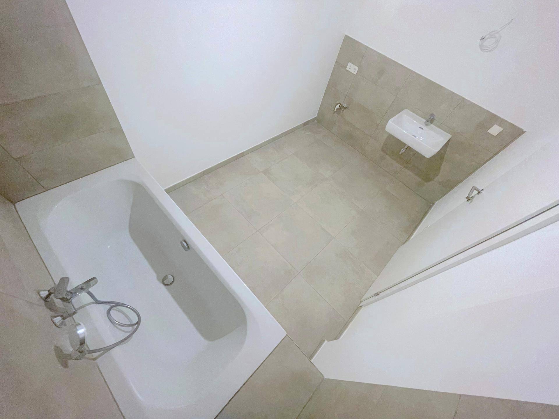 Modernes Badezimmer mit Badewanne, Einzelwaschbecken und hellen Fliesen, in neuwertigem Zustand.