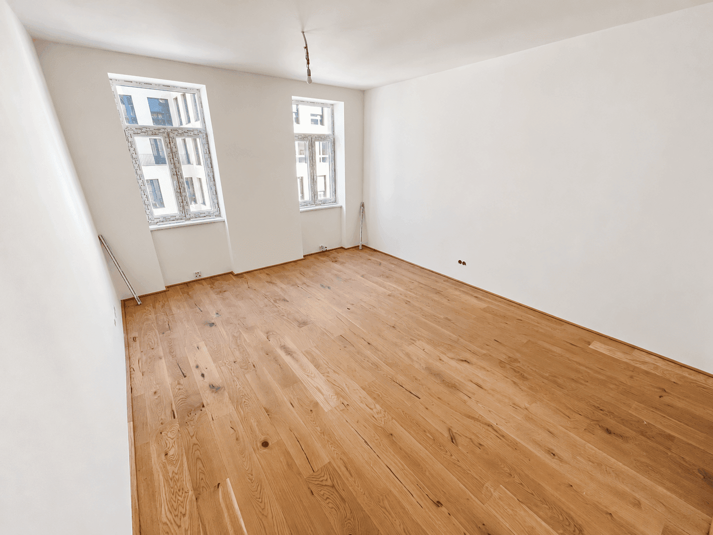 Lichtdurchfluteter Raum mit frisch verlegtem Holzplankenboden und weiß gestrichenen Wänden.