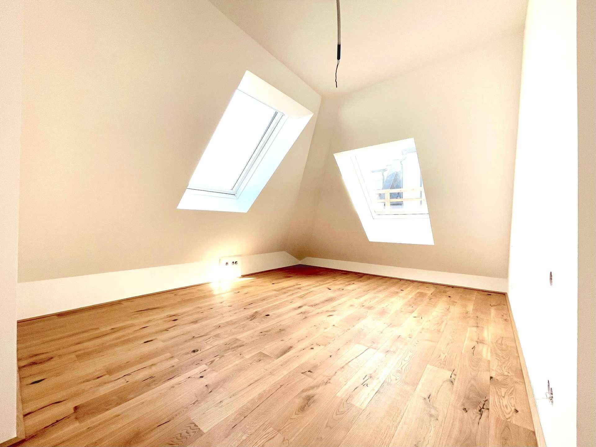 Helles Zimmer mit Holzboden und zwei Dachfenstern, das viel natürliches Licht hereinlässt.