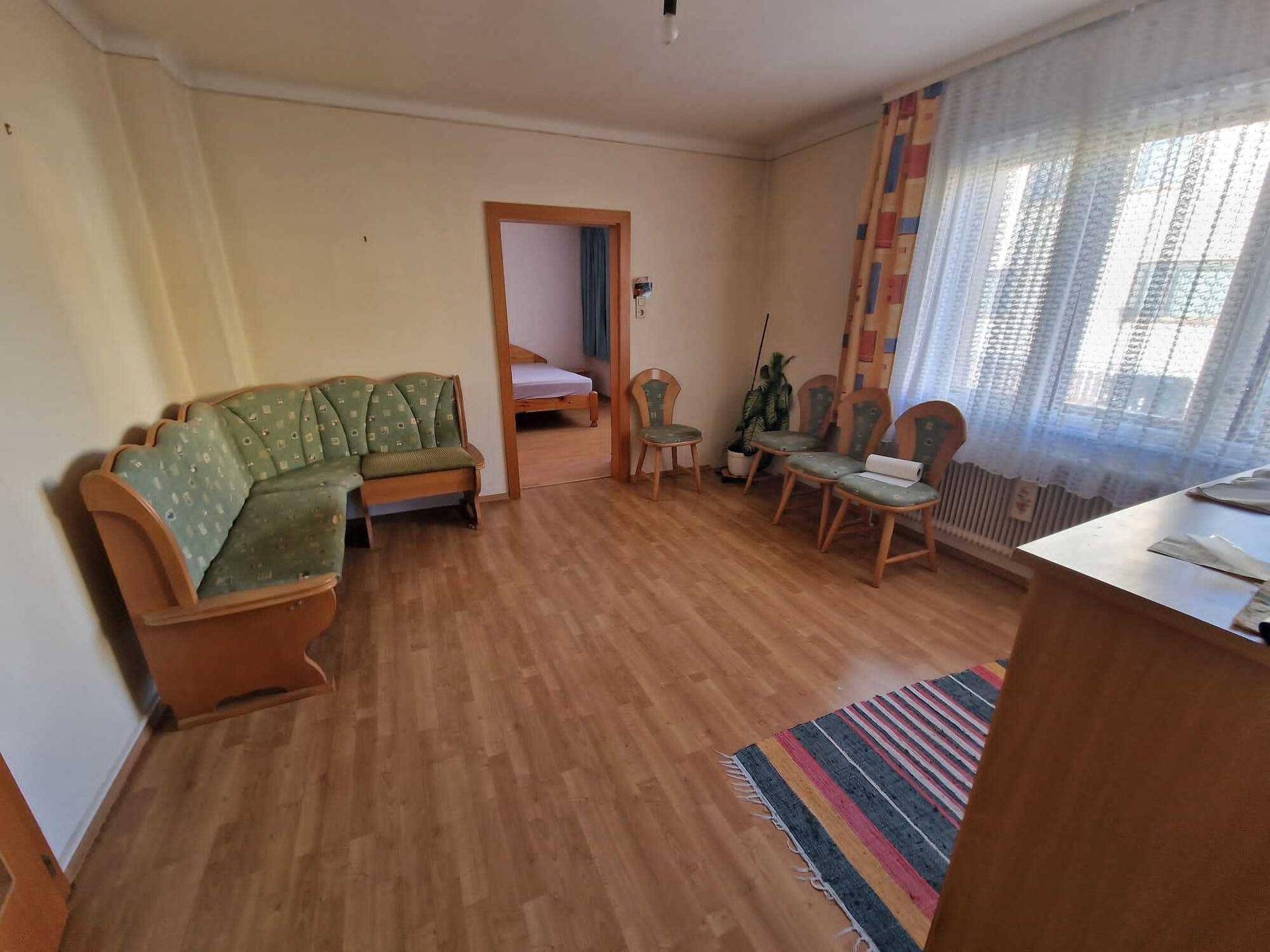 Helles Wohnzimmer mit Laminatboden, Ecksofa und Zugang zu einem weiteren Raum.
