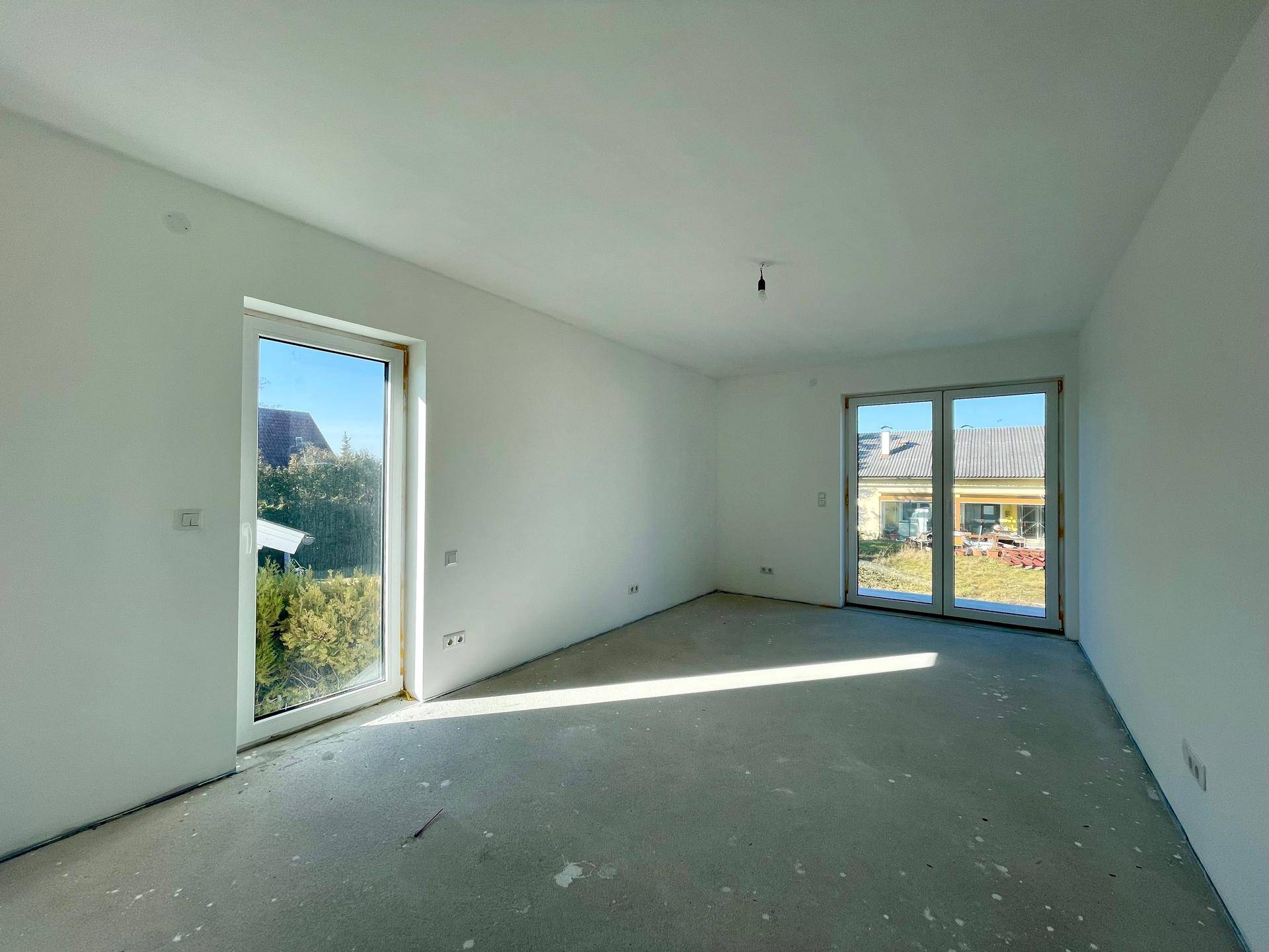 Heller Raum im Rohbau mit zwei großen Fenstertüren, die viel Licht hereinlassen.
