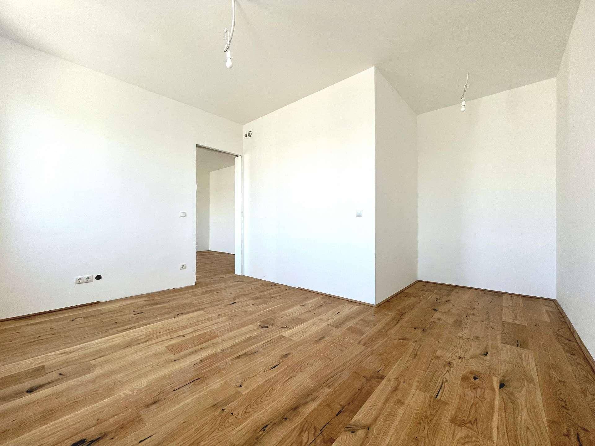 Geräumiger, unmöblierter Wohnbereich mit Holzboden und Zugang zu weiteren Zimmern.