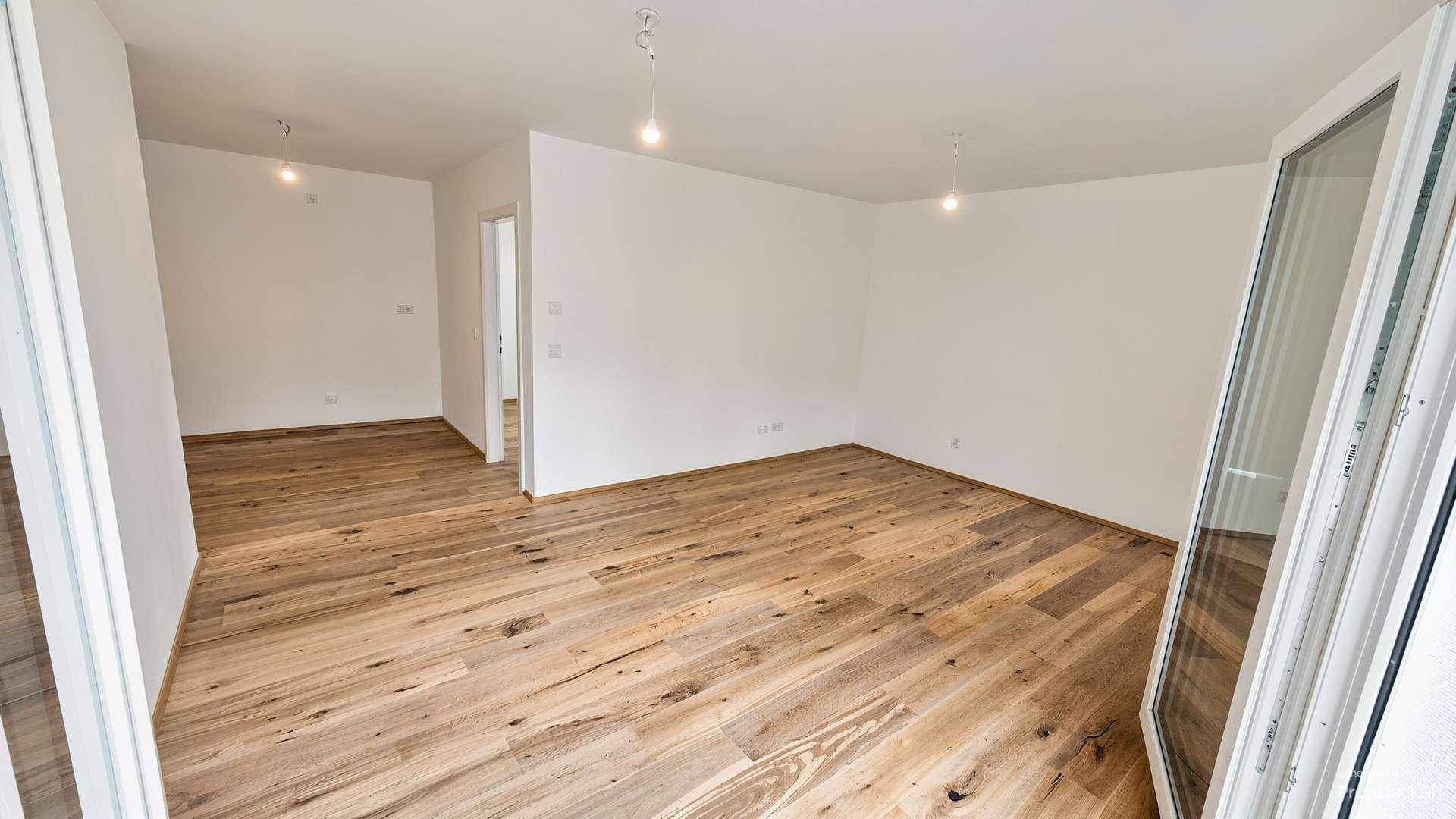 Heller Raum mit schönem Holzboden und weiß gestrichenen Wänden, bietet Zugang zu weiteren Zimmern.