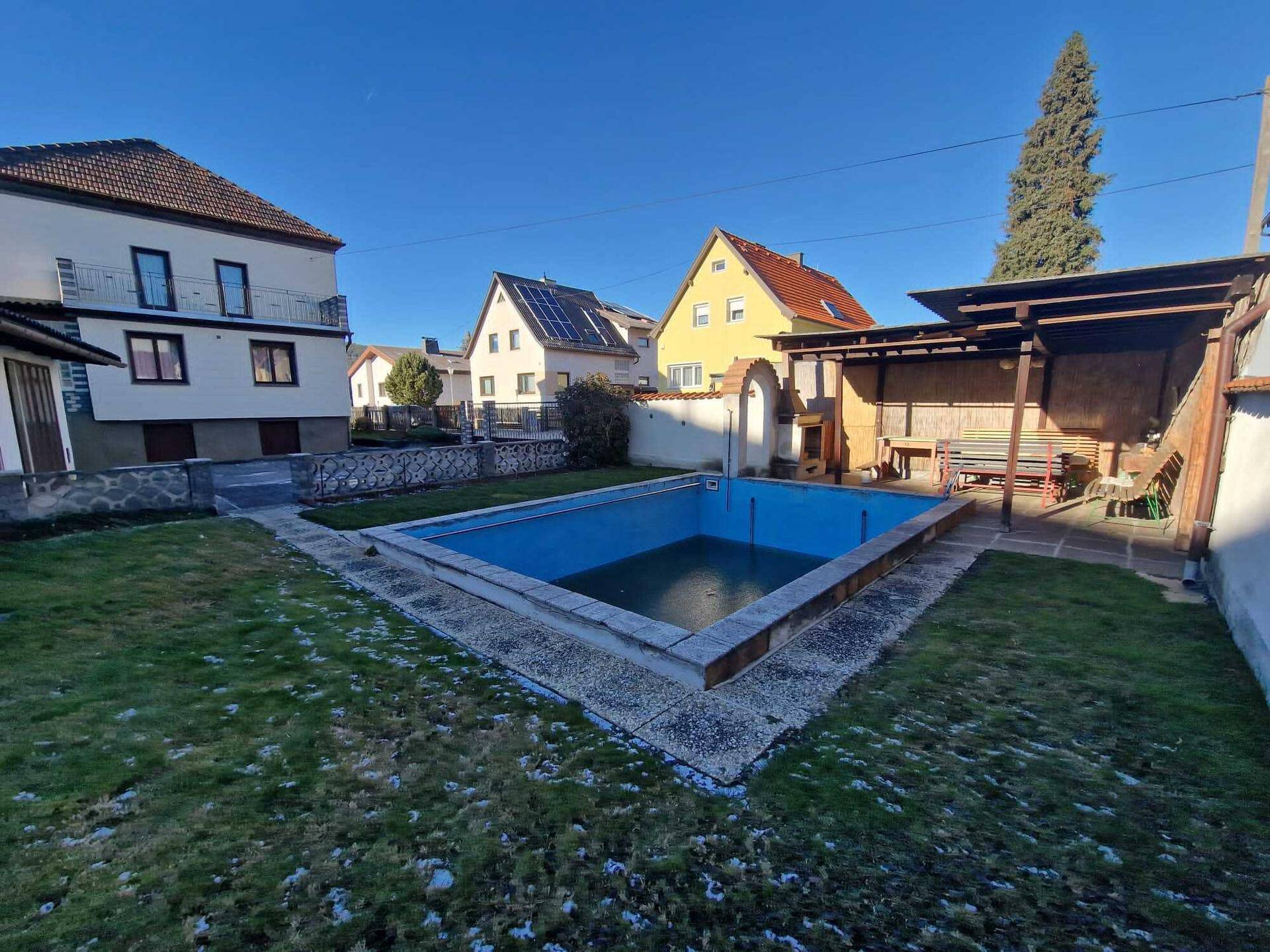 Großer Gartenbereich mit einem leeren Swimmingpool und einer überdachten Sitzecke.
