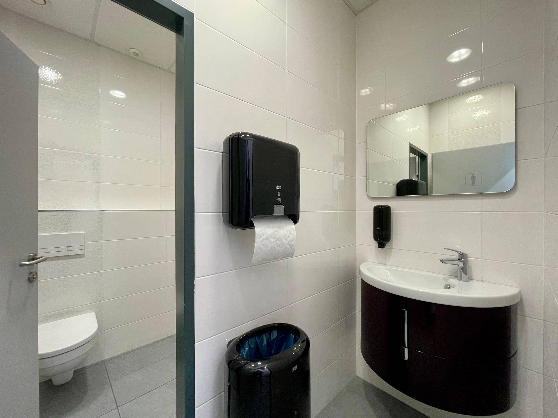 Modernes Badezimmer mit weißen Fliesen, dunklem Waschtisch und einer wandhängenden Toilette, sehr gepflegt.