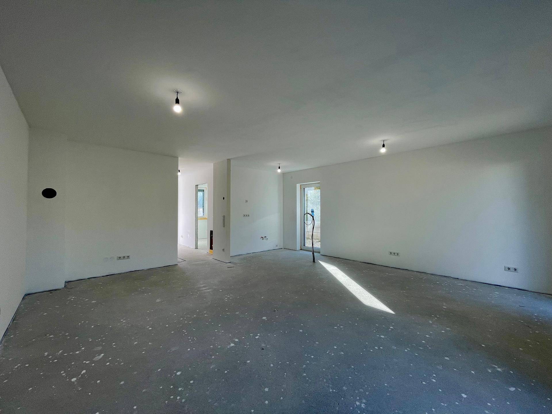 Weitläufiger, heller Innenraum im Rohbau mit mehreren Türöffnungen und Betonboden.