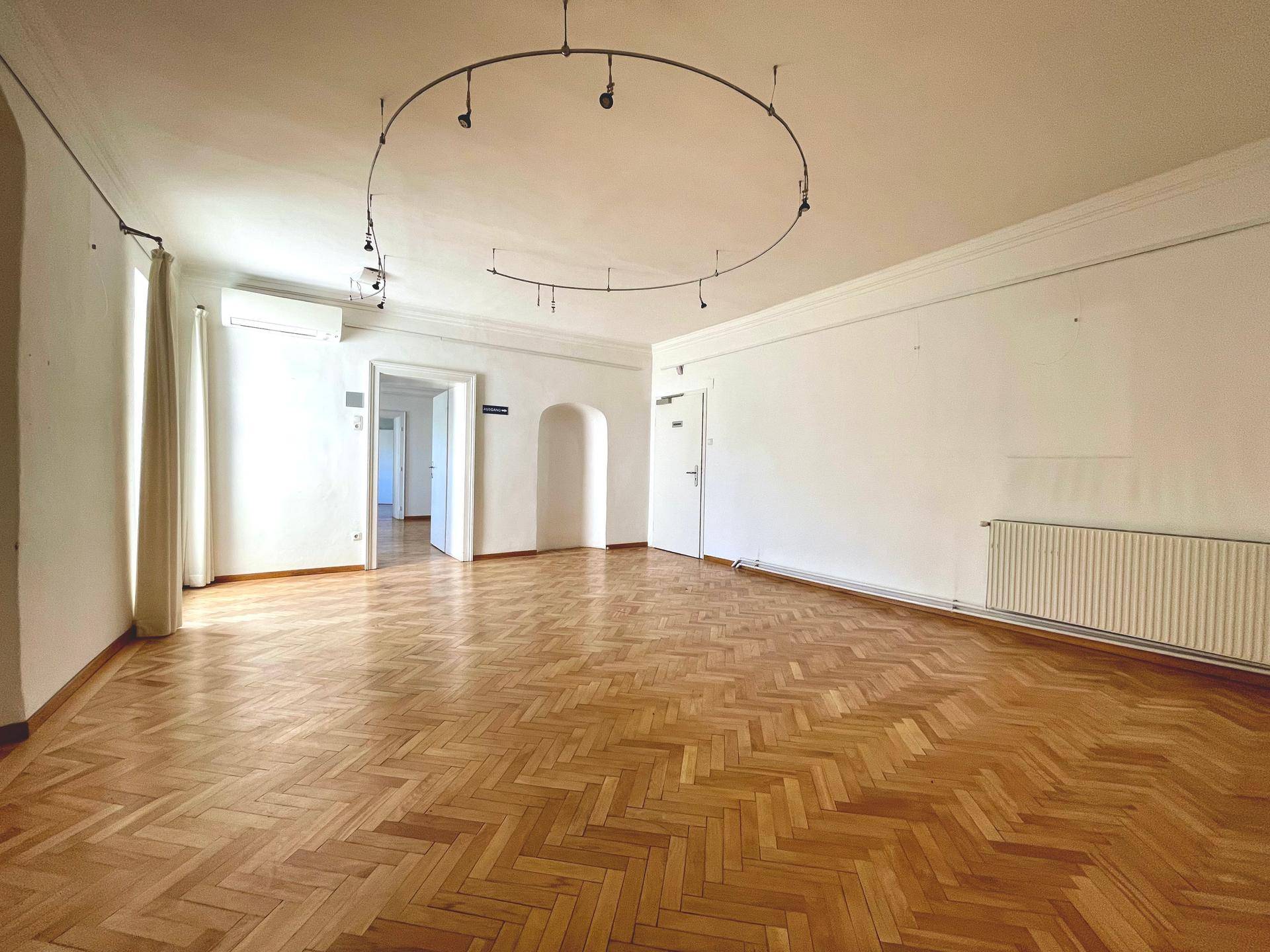 Geräumiger Raum mit Fischgrätparkett, hohen Decken, Klimaanlage und einem Heizkörper an der Wand.
