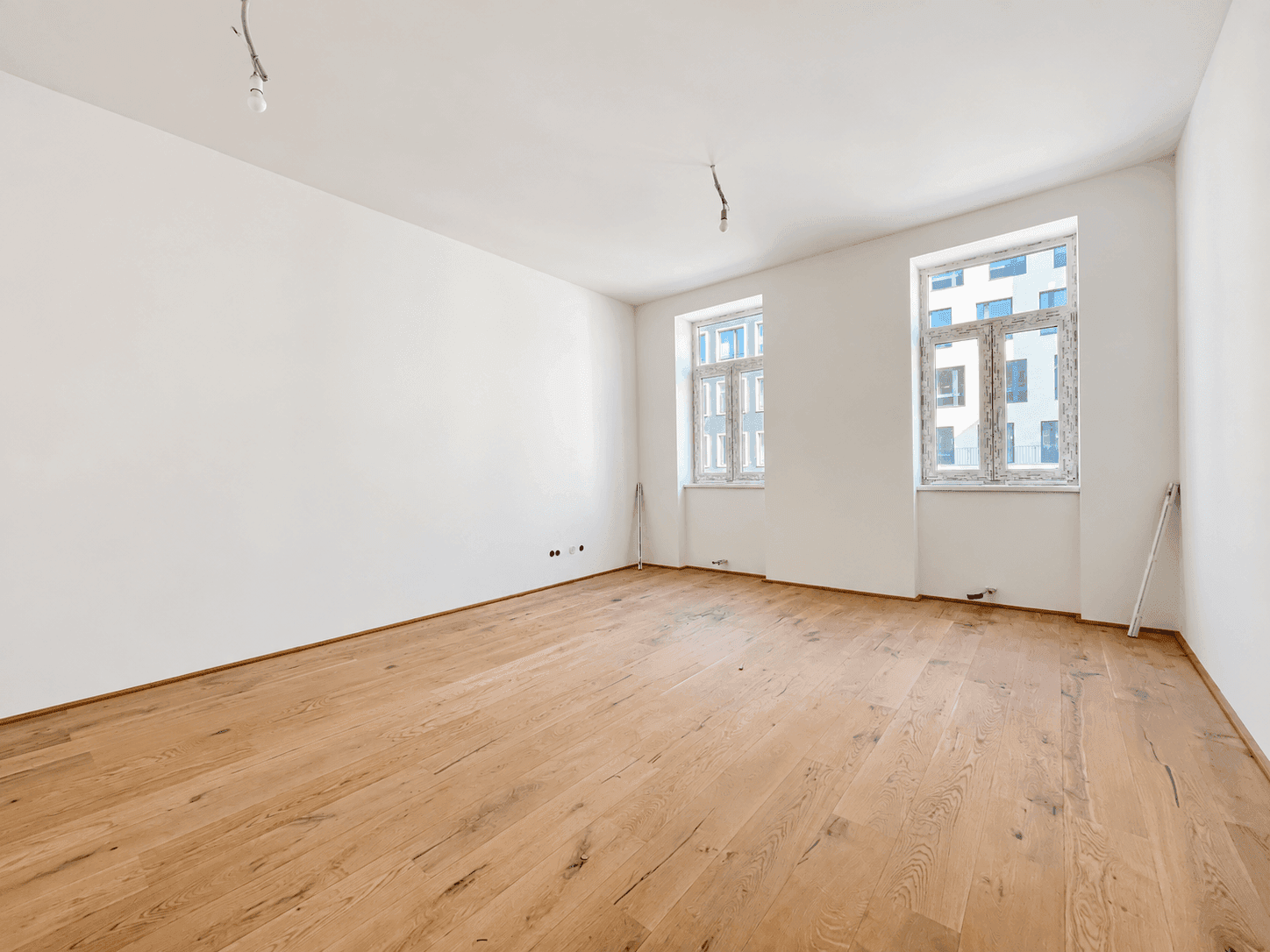 Heller, leerer Raum mit neuem Holzboden und zwei Fenstern, ideal für Wohn- oder Schlafbereich.