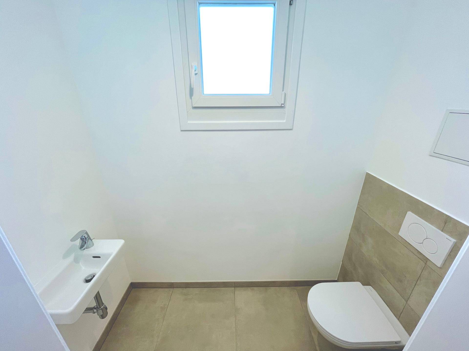 Separates Gäste-WC mit Wand-WC, kleinem Waschbecken und Fenster, in modernem Design.