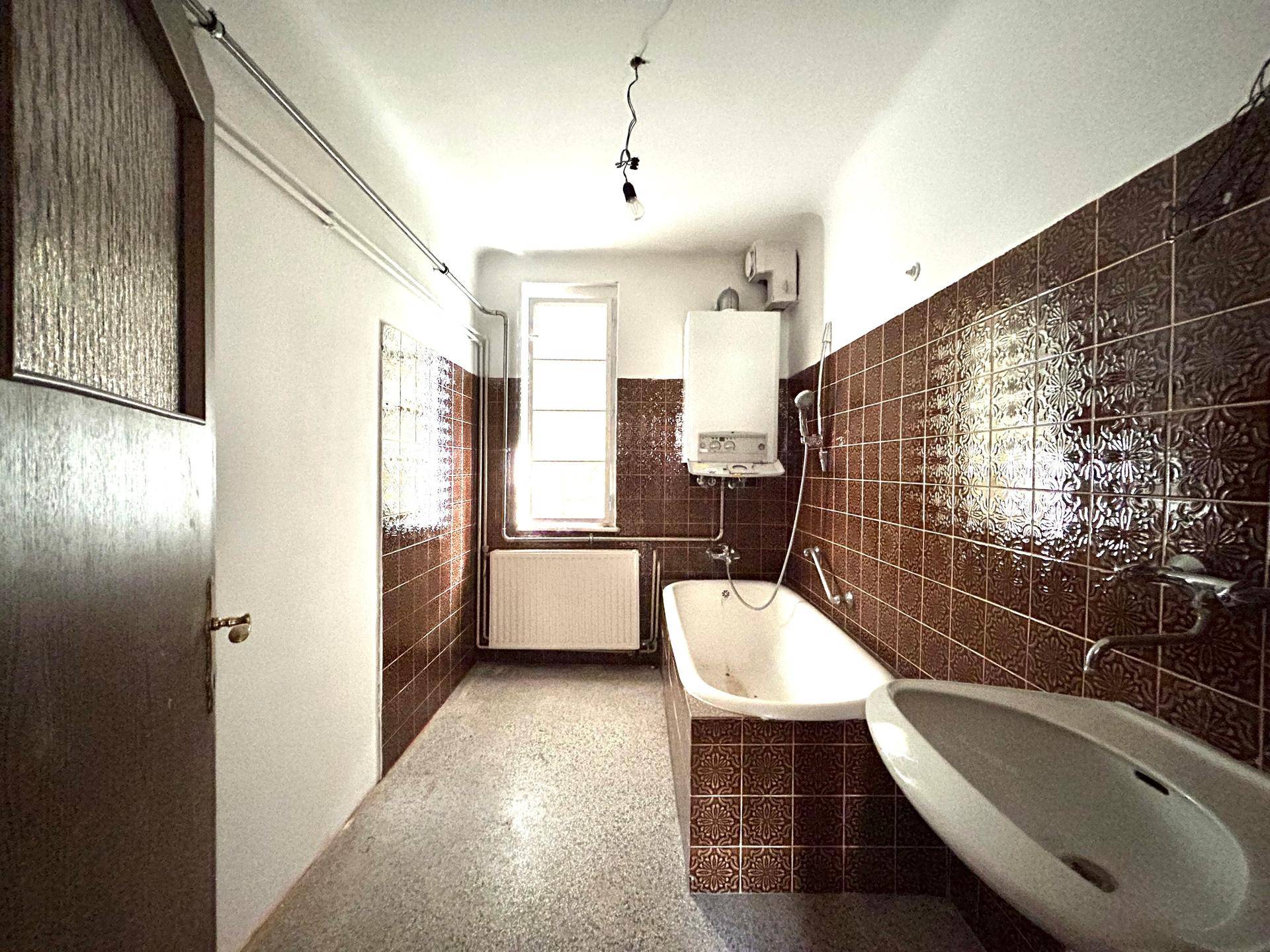 Badezimmer mit braunen Fliesen, Badewanne, Waschbecken und einem Fenster, typisch für die 80er Jahre.