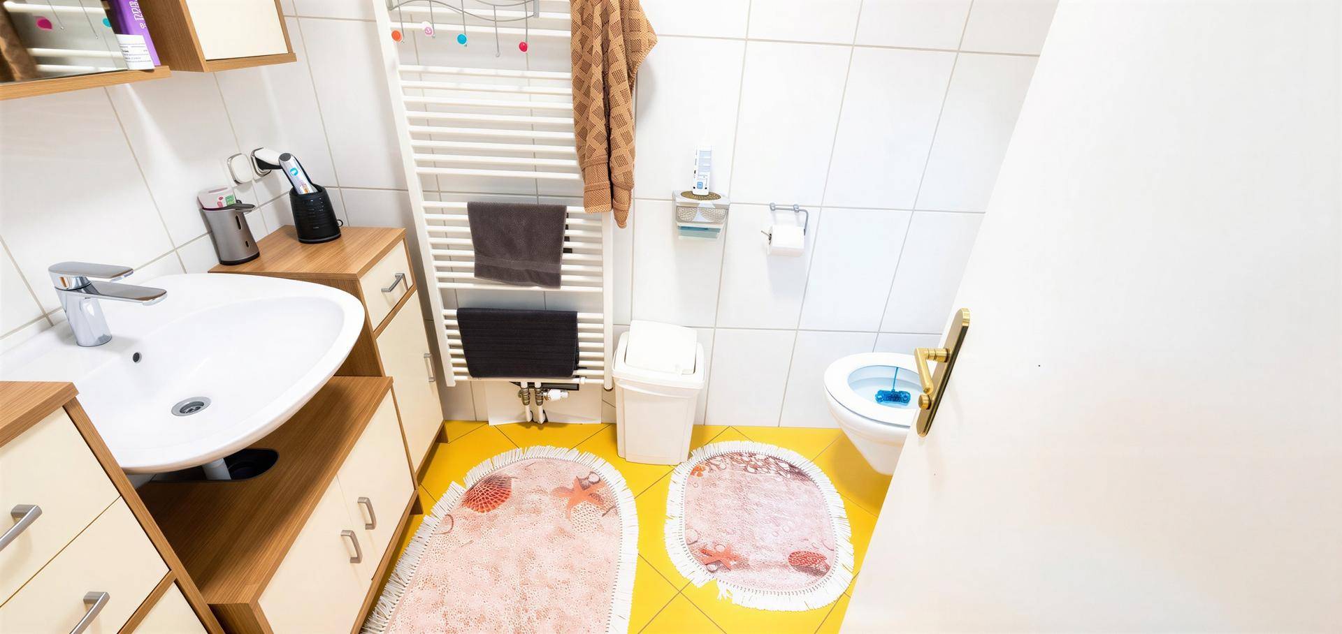Helles Badezimmer mit gelben Fliesen, Einzelwaschbecken, Toilette und Handtuchheizkörper.