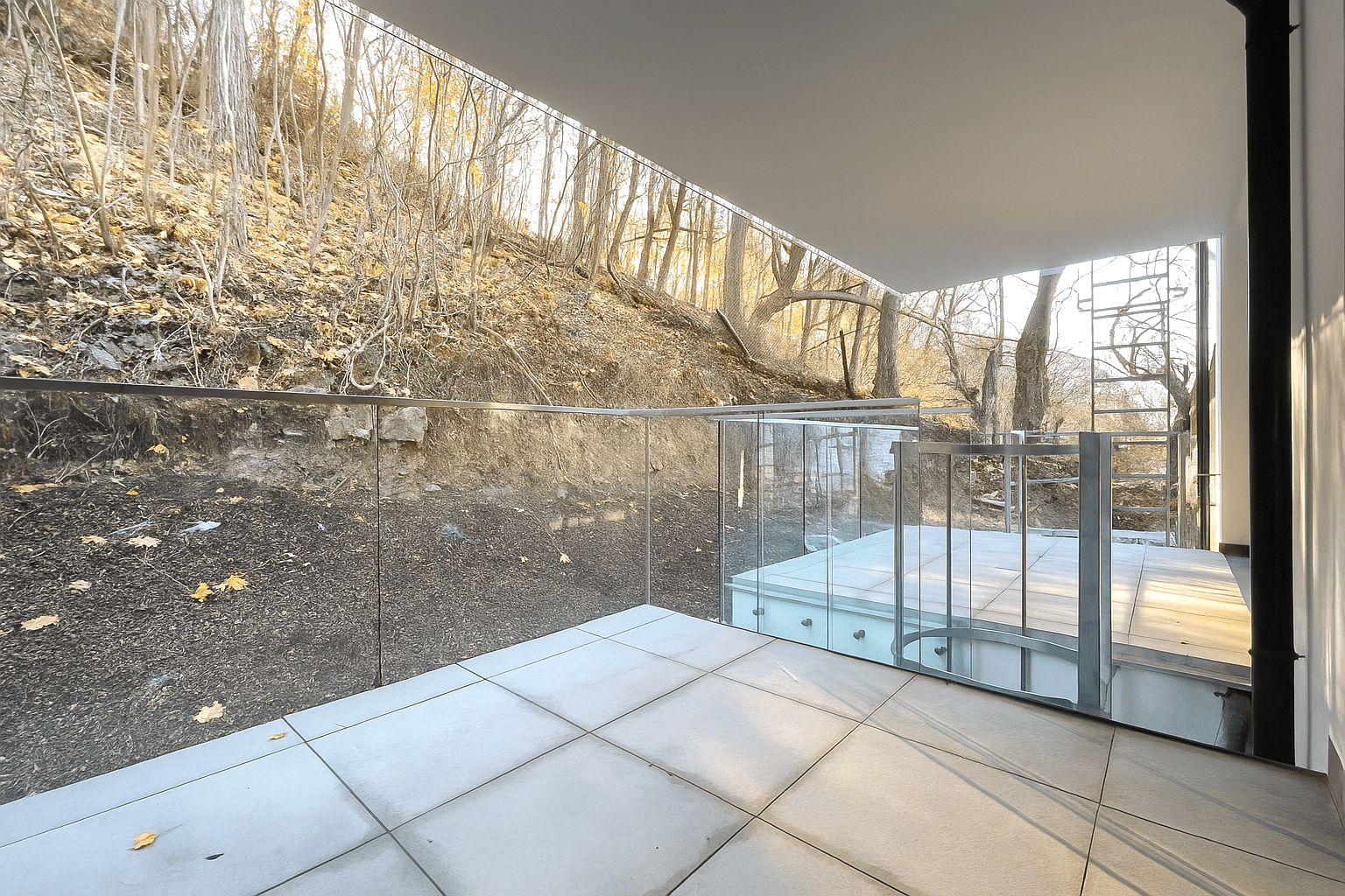 Moderne Terrasse mit Glasgeländer und Blick auf einen bewaldeten Hang.
