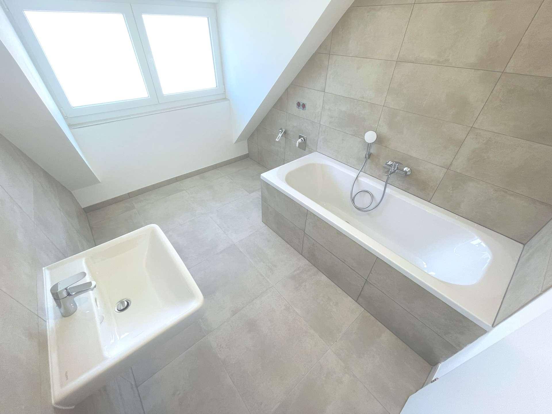 Modernes Badezimmer mit Badewanne, Waschbecken und Fenster, unter einer Dachschräge gelegen.