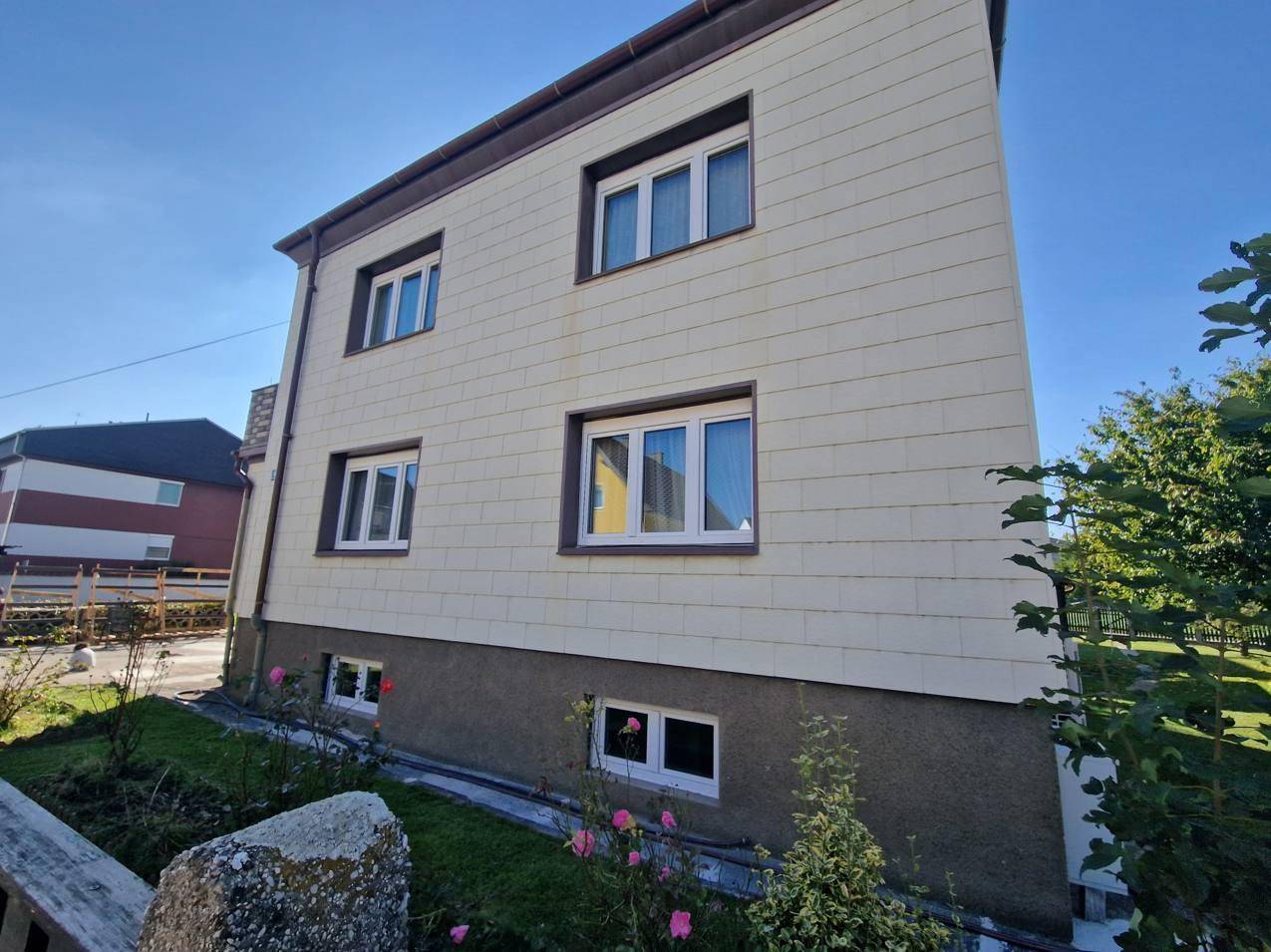 Seitenansicht des Hauses mit heller Fassade, weißen Fenstern und blühenden Rosen im Vorgarten.
