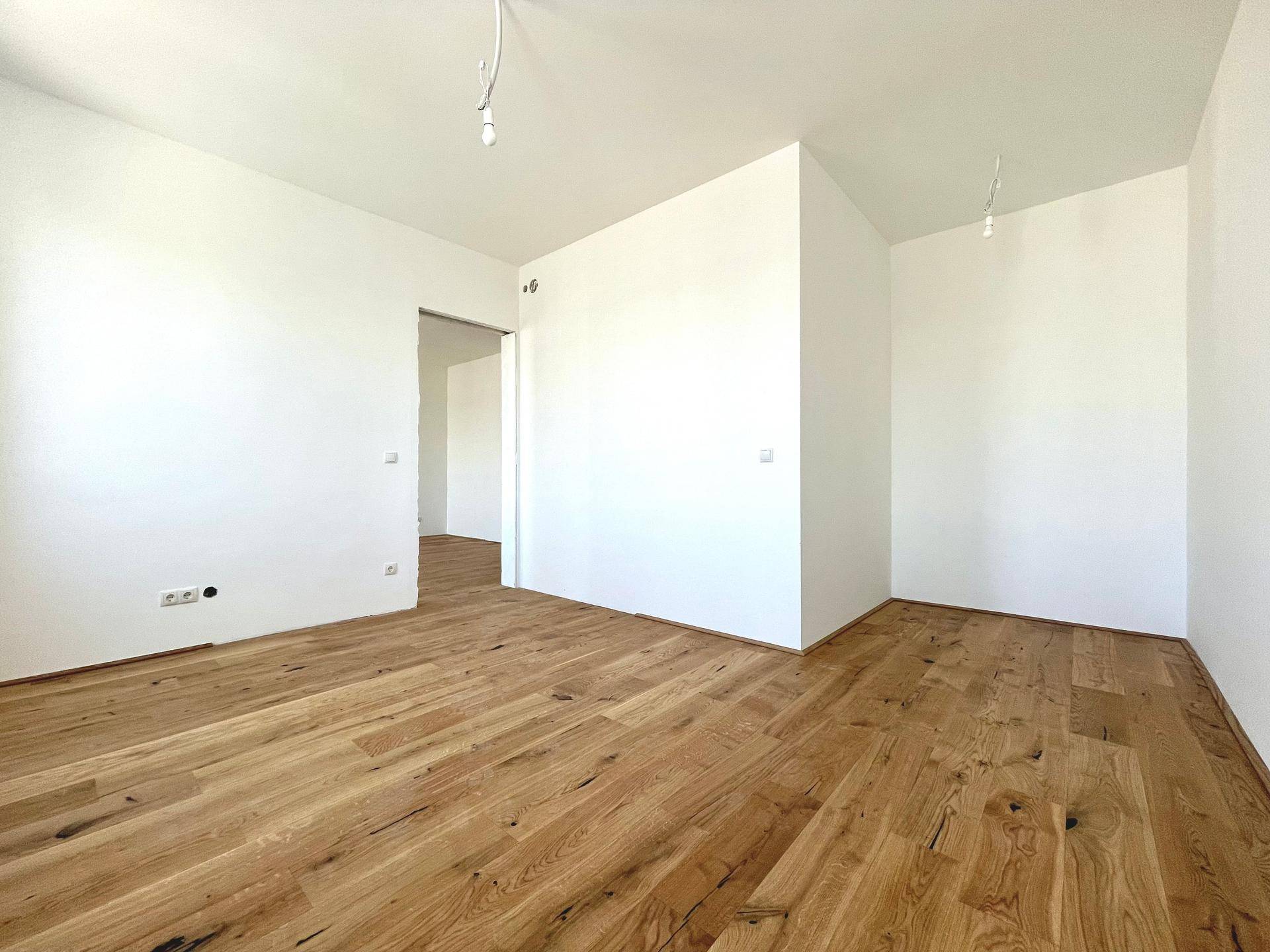 Geräumiges Zimmer mit neu verlegtem Holzboden und weißen Wänden, ideal für verschiedene Nutzungsmöglichkeiten.