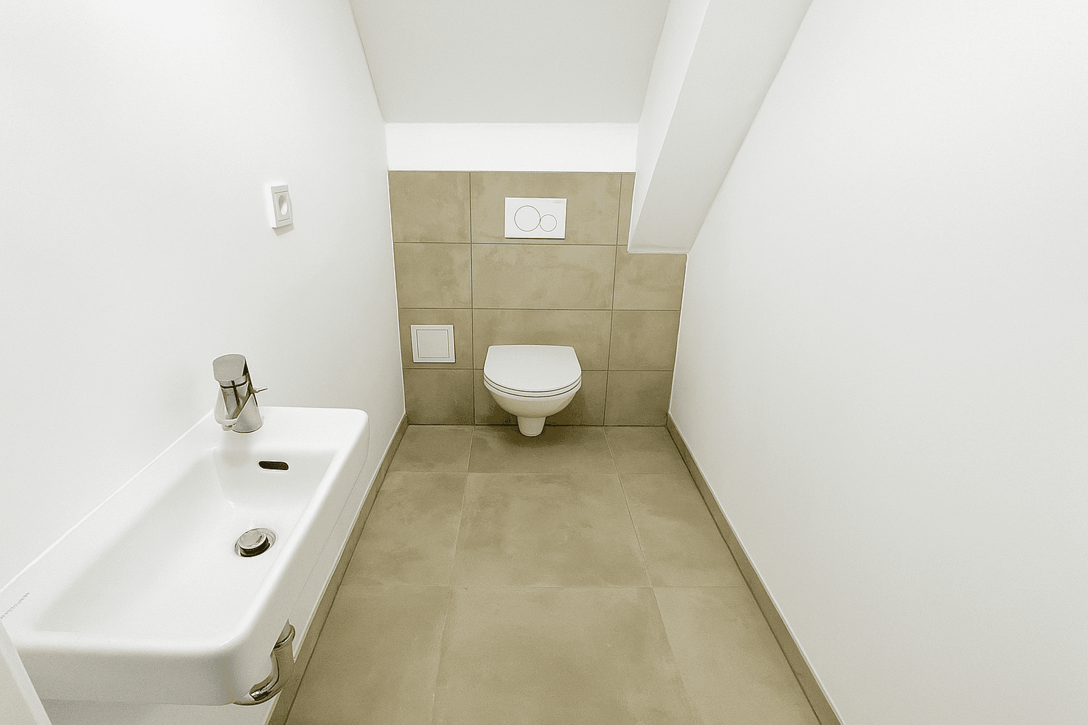 Kleines Gäste-WC mit Wand-WC, Waschbecken und modernen Fliesen unter einer Dachschräge.