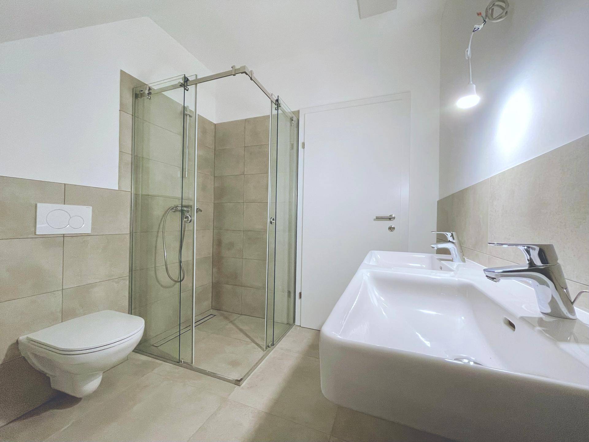 Geräumiges Badezimmer im Dachgeschoss mit Duschkabine, Wand-WC und Doppelwaschbecken, in modernem Design.