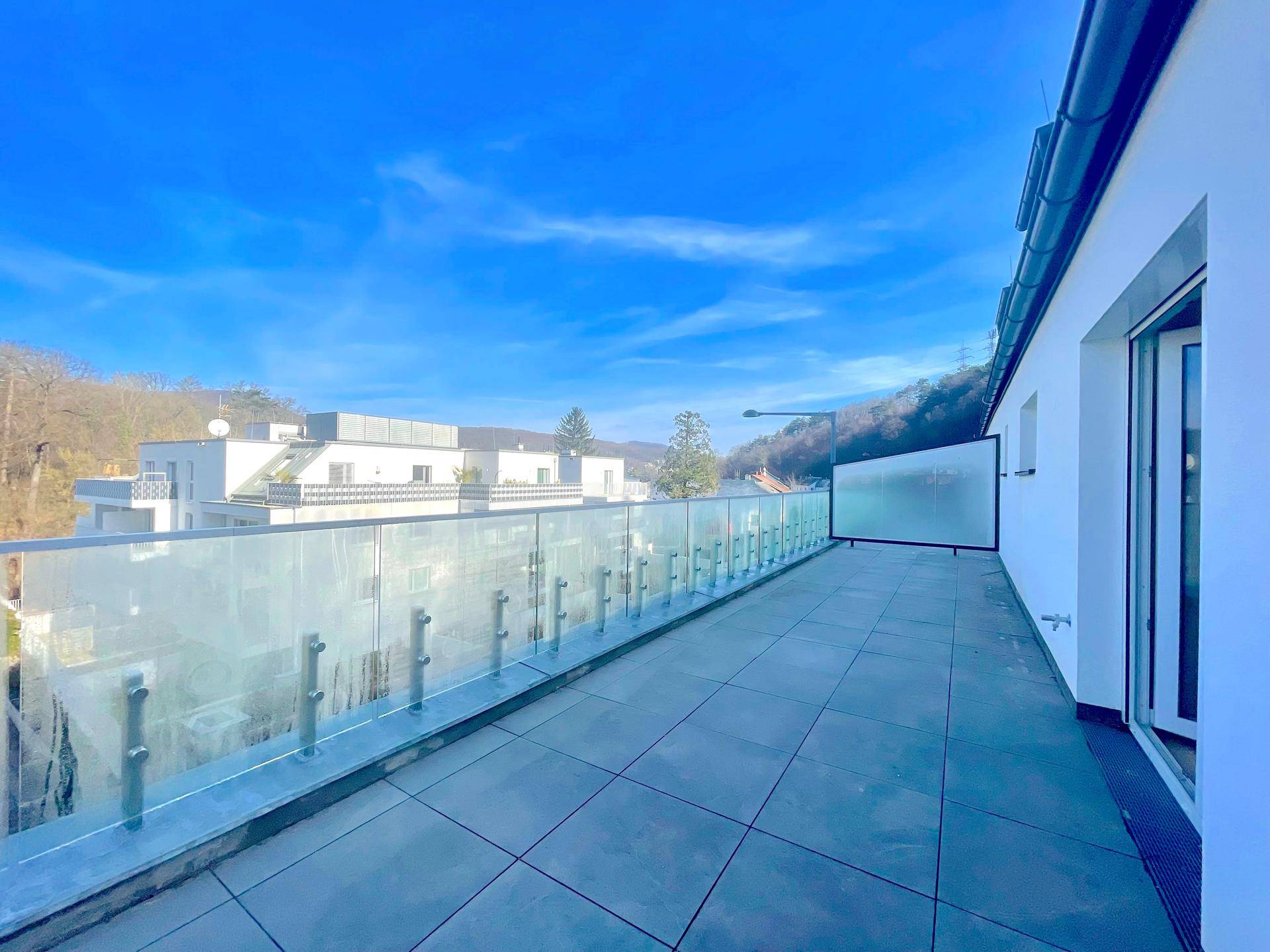 Große Dachterrasse mit Fliesenboden und Glasgeländer, bietet einen weiten Blick auf die umliegende Landschaft.