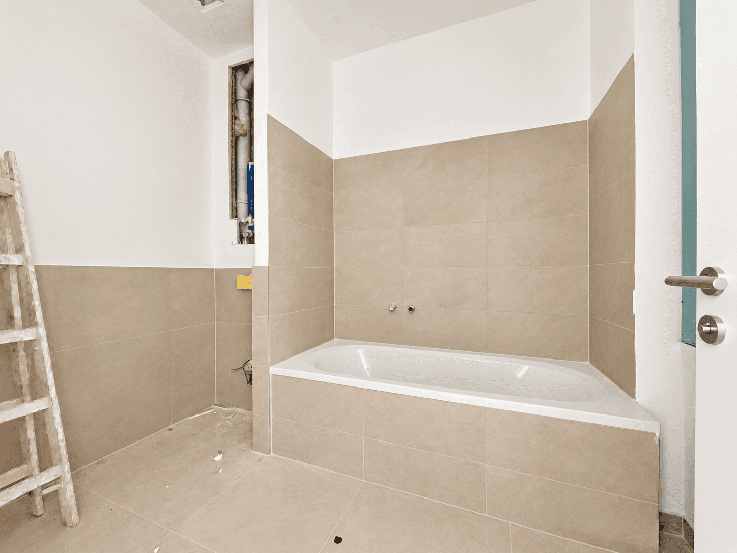 Badezimmer im Bau mit eingebauter Badewanne und beigefarbenen Fliesen, bereit für die Fertigstellung.