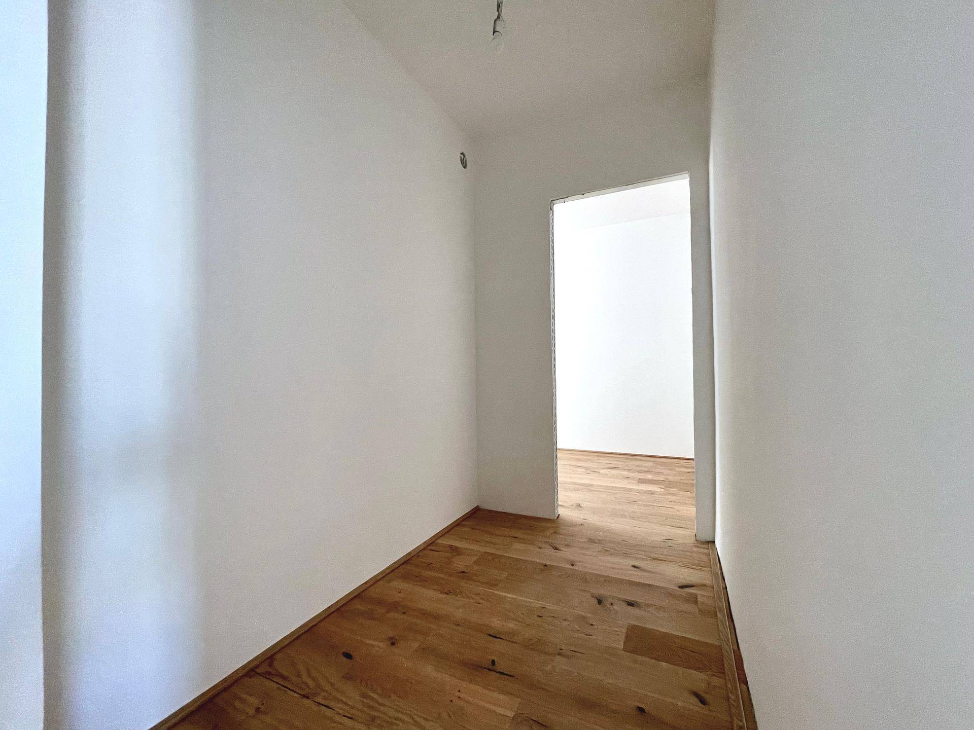 Heller Flur mit neuem Holzparkettboden, der zu weiteren Räumen führt.