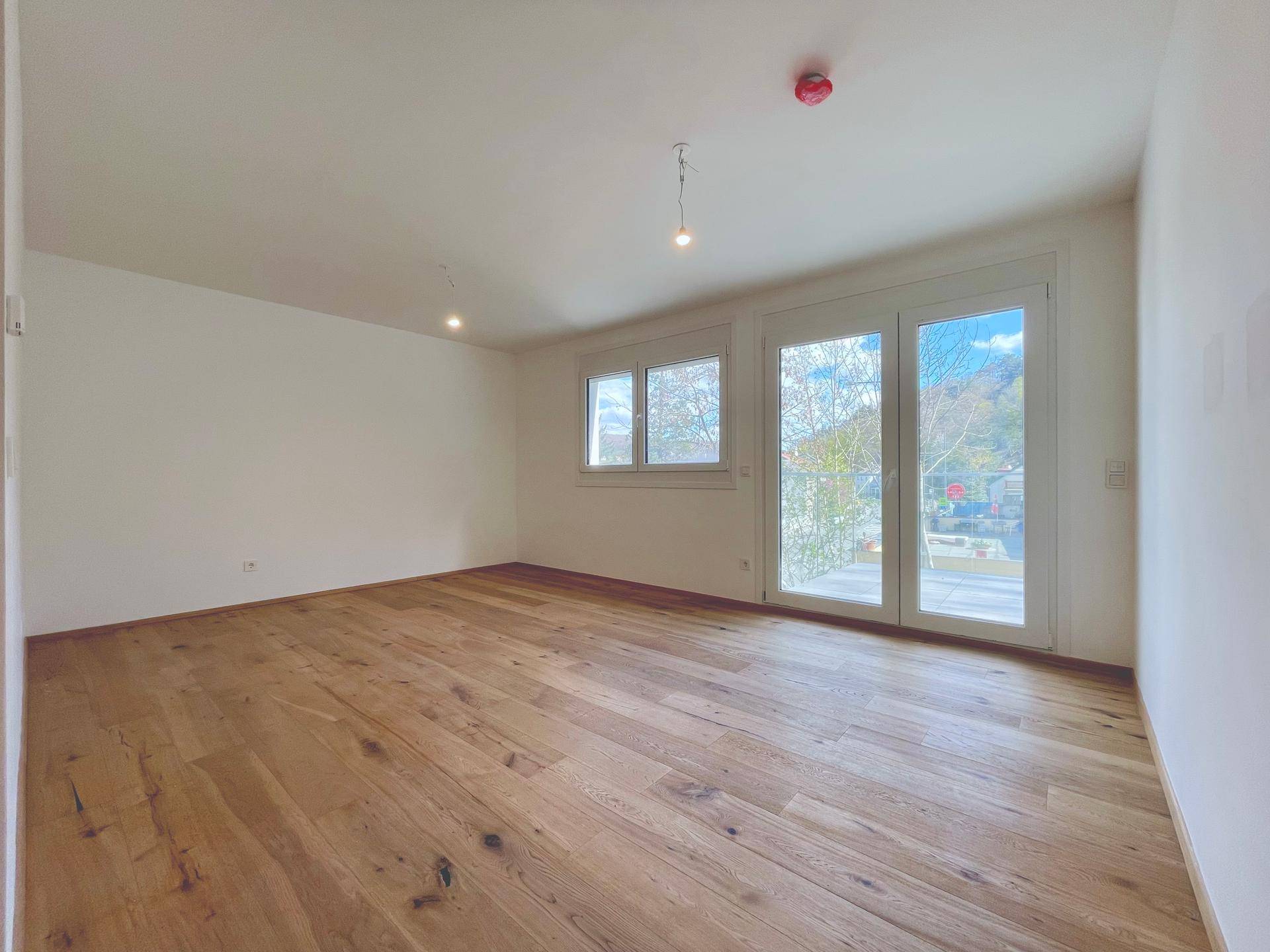 Geräumiges Wohnzimmer mit Holzboden und großen Fenstern, bietet viel Tageslicht und frische Luft.