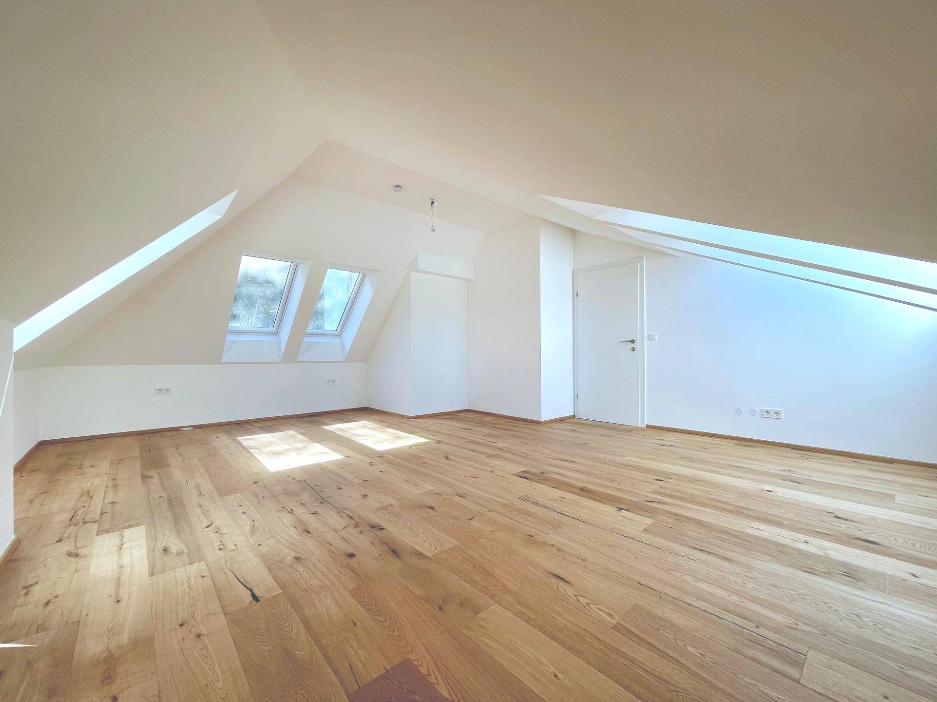 Lichtdurchflutetes Wohnzimmer im Dachgeschoss mit Holzboden und Dachfenstern, ideal für offenes Wohnen.