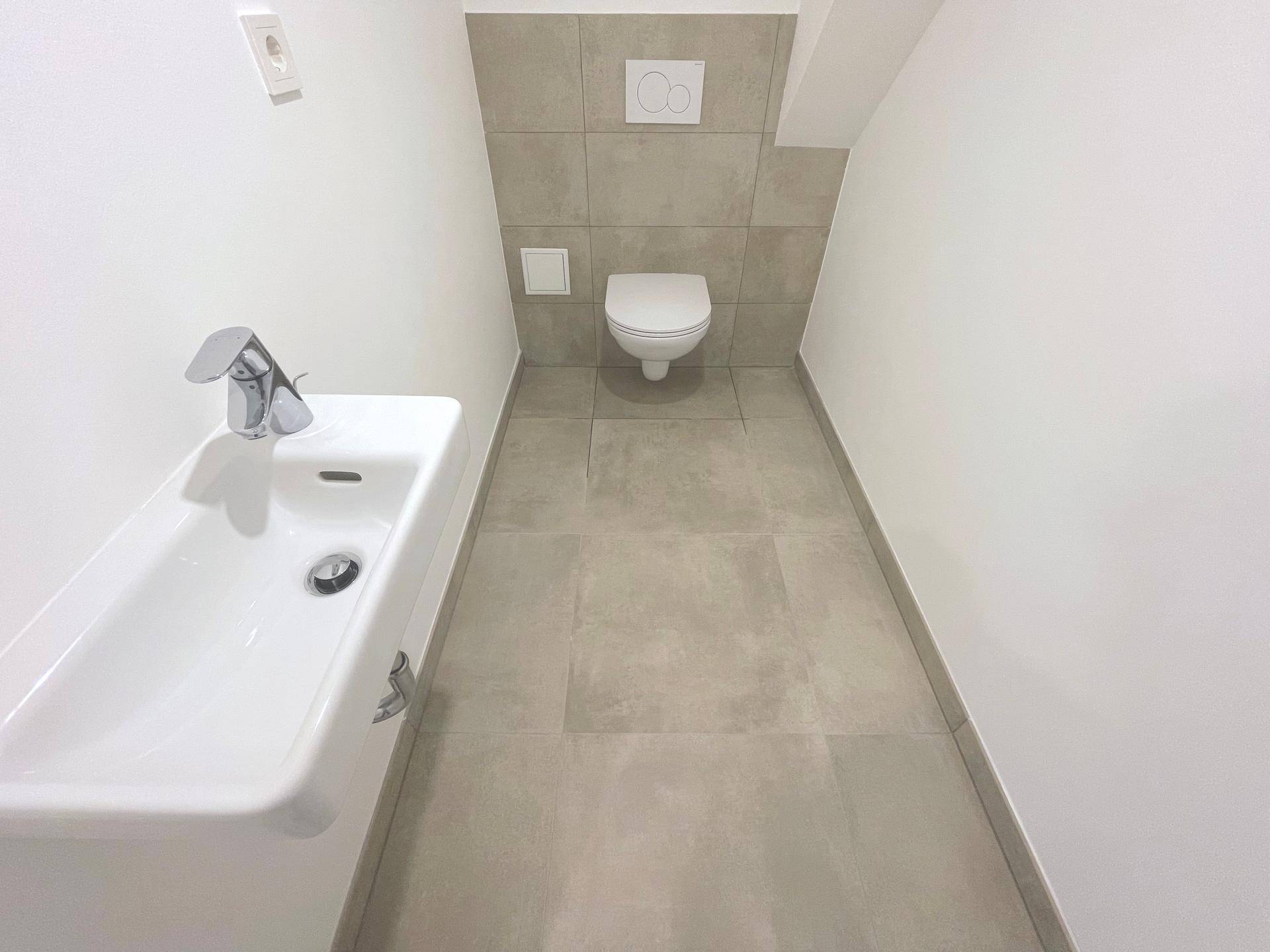 Separates Gäste-WC im Dachgeschoss mit Wand-WC, kleinem Waschbecken und Fenster, in modernem Design.