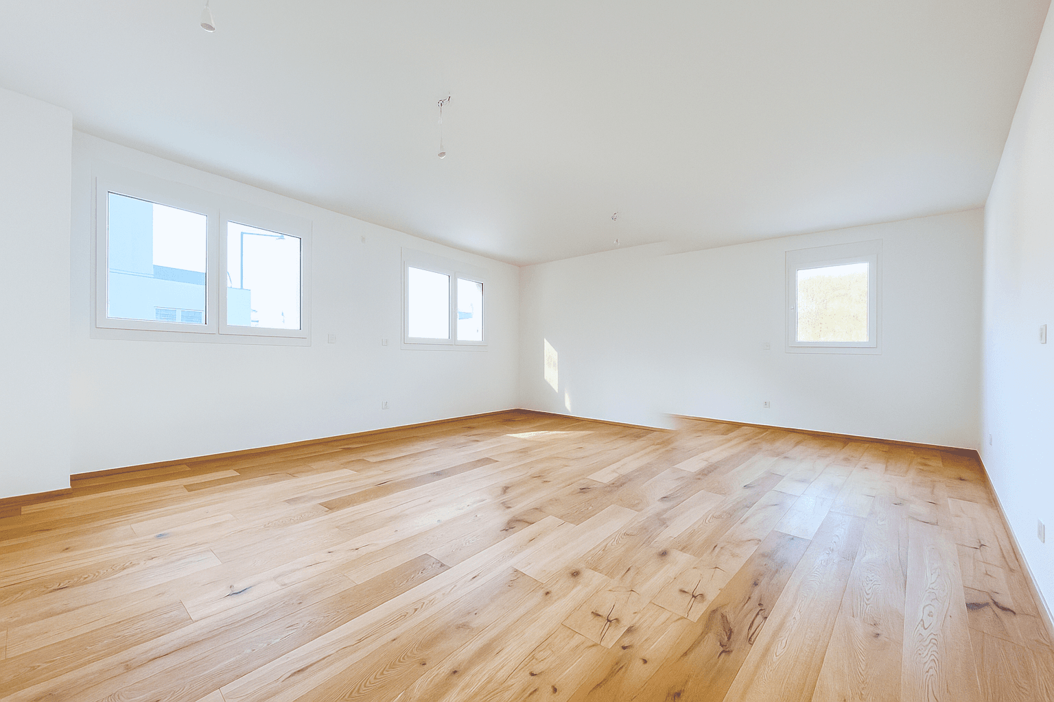 Großzügiges, lichtdurchflutetes Wohnzimmer mit Holzboden und vielen Fenstern, ideal für offenes Wohnen.