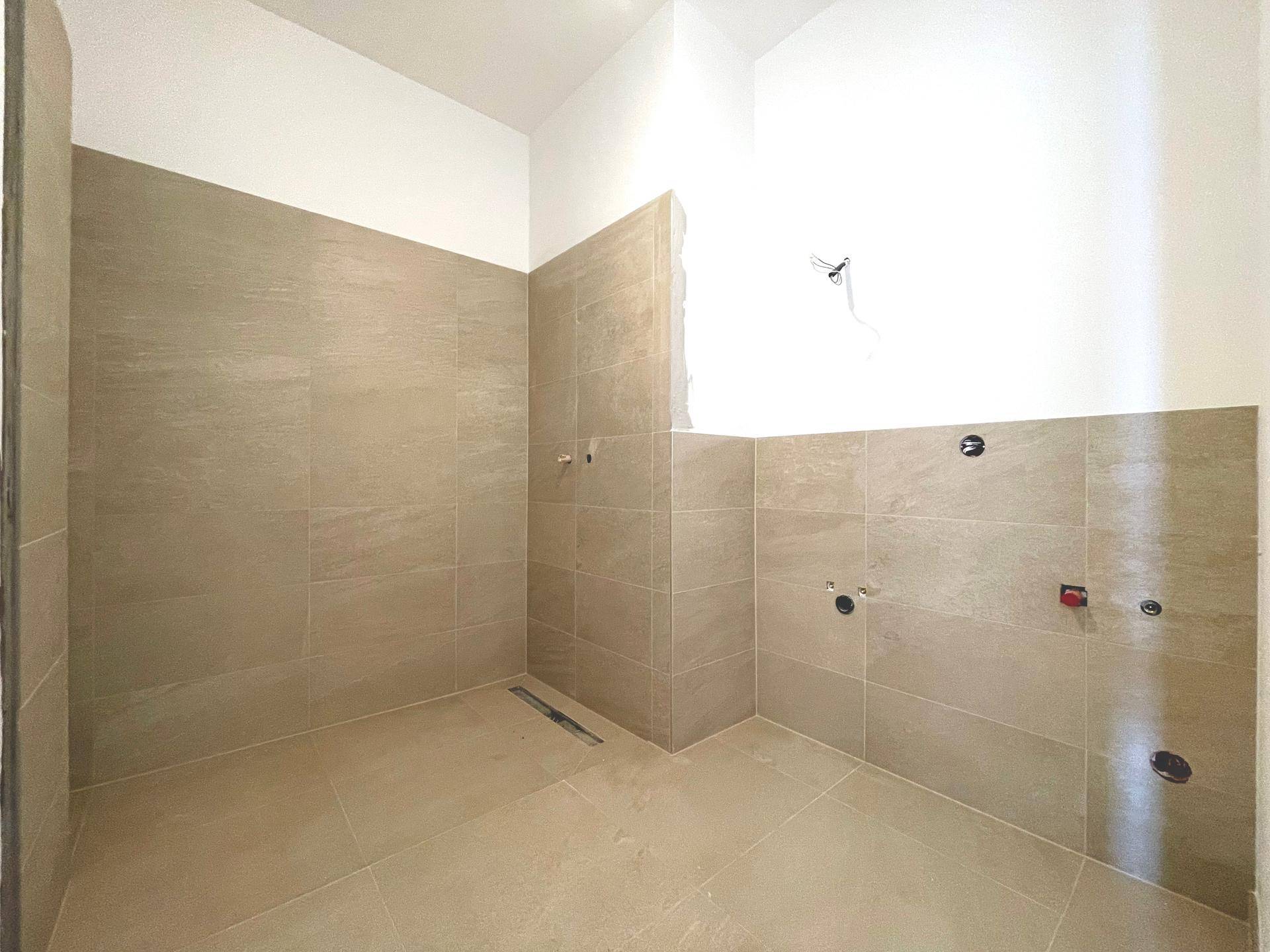 Badezimmer im Bau mit beigefarbenen Fliesen an Wänden und Boden, vorbereitet für Installationen.