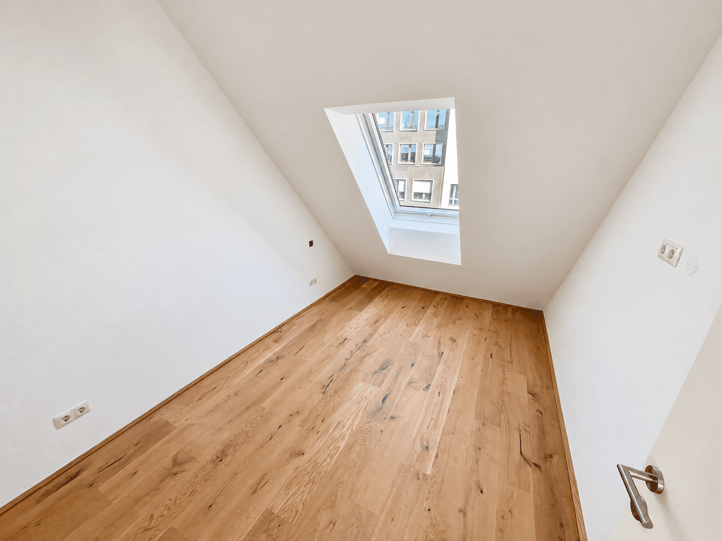 Kleineres Zimmer mit Holzboden und einem Dachfenster, geeignet als Kinder- oder Gästezimmer.