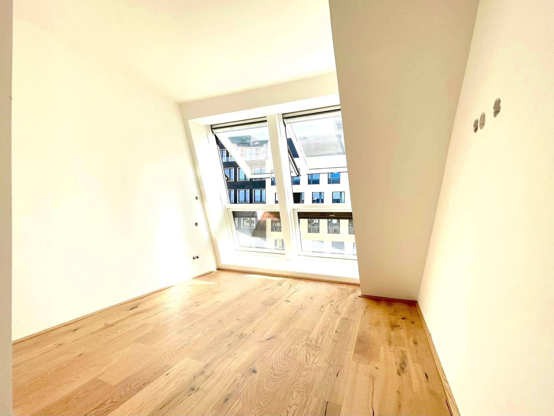 Helles Zimmer mit Holzboden und großen Fenstern, die einen Blick auf die Umgebung ermöglichen.