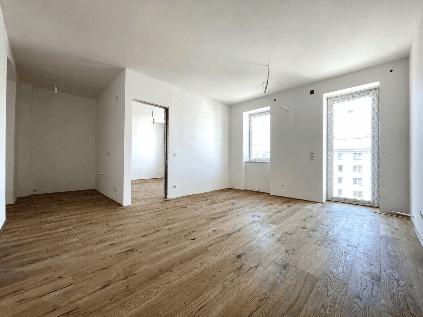 Geräumiger Wohnbereich mit Holzboden und hohen Fenstern, bietet viel Platz für individuelle Gestaltung.