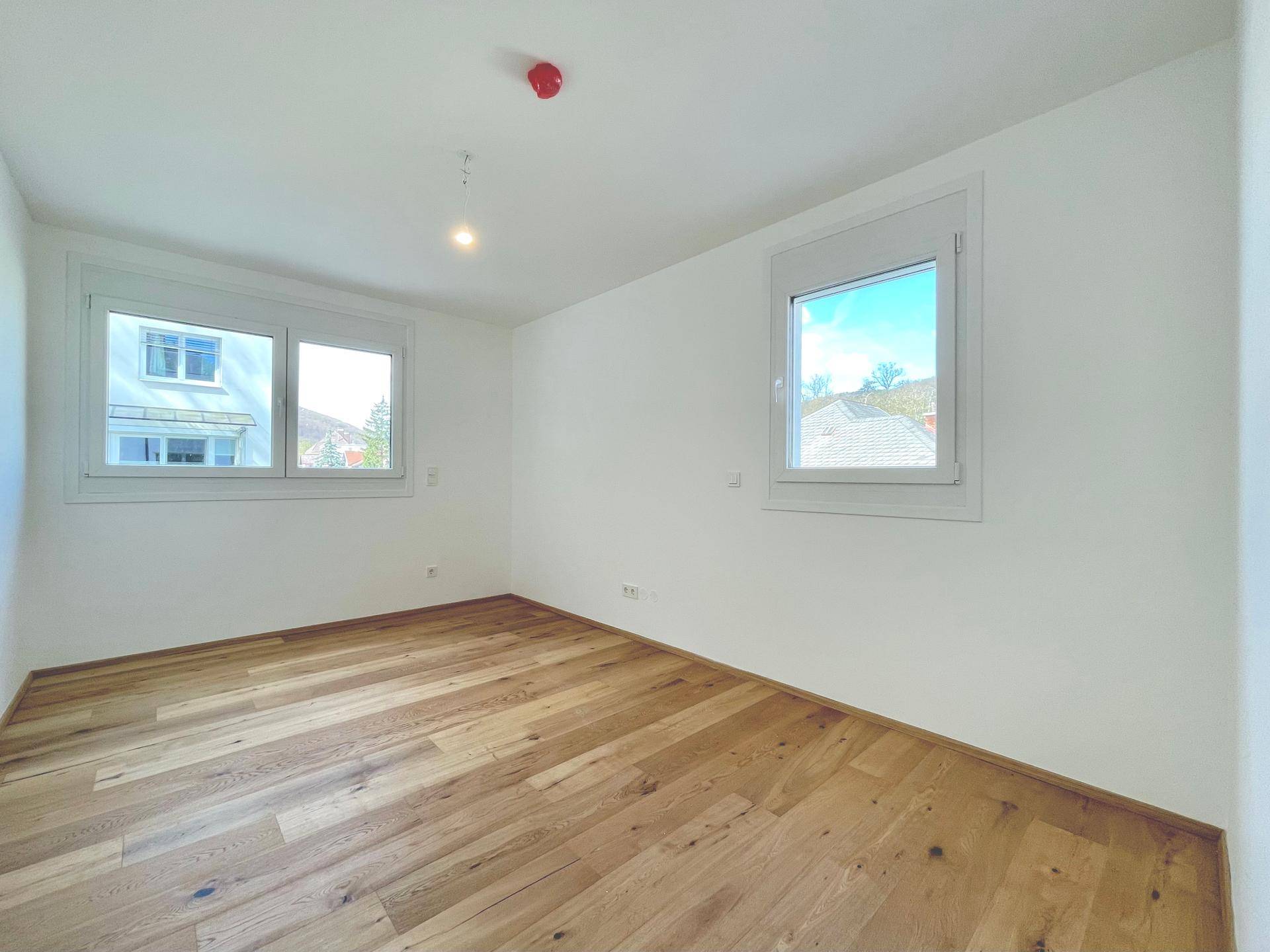 Helles Schlafzimmer mit zwei Fenstern und Holzboden, bietet viel Tageslicht.