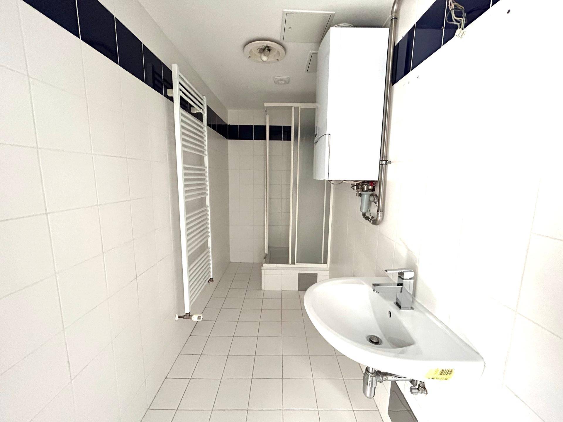 Gefliestes Badezimmer mit Dusche, Waschbecken, Handtuchheizkörper und Gastherme.