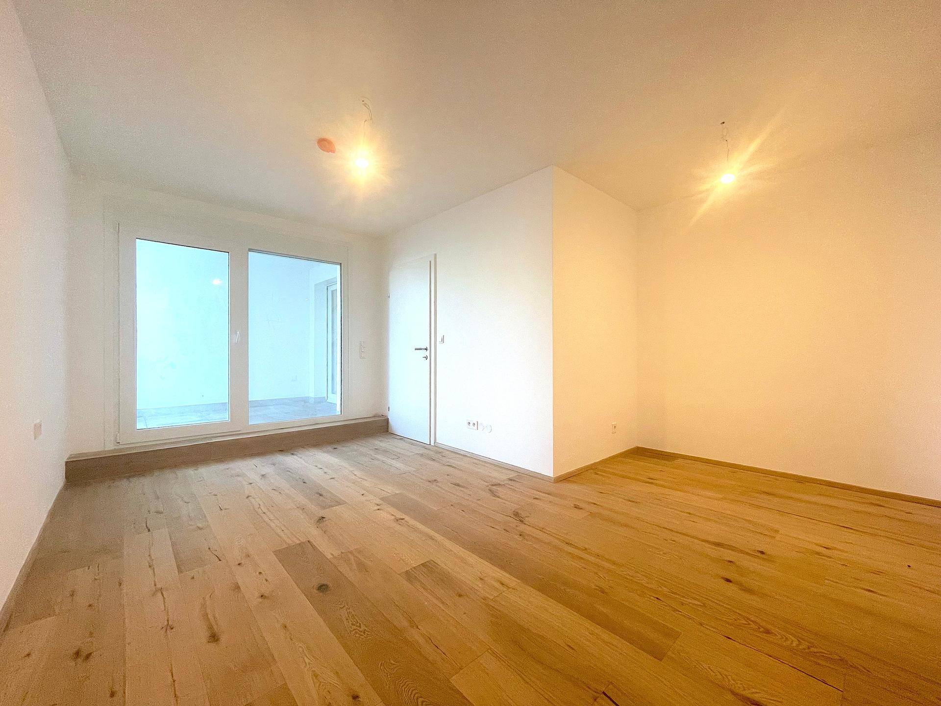 Helles Wohnzimmer mit Holzboden und mehreren Fenstern, bietet viel Tageslicht und eine offene Atmosphäre.