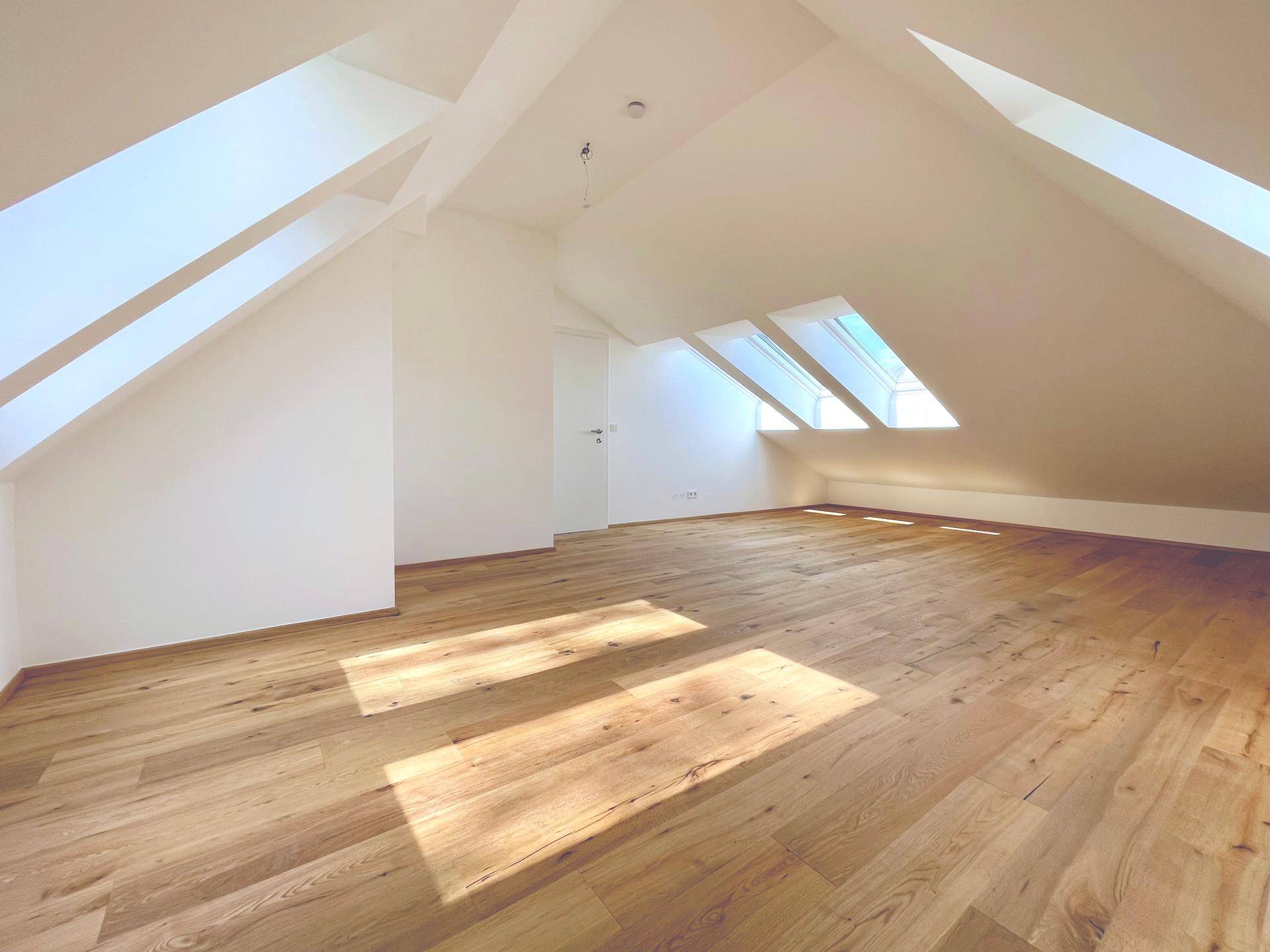 Geräumiges Wohnzimmer im Dachgeschoss mit Holzboden und Dachfenstern, bietet eine helle Wohnatmosphäre.