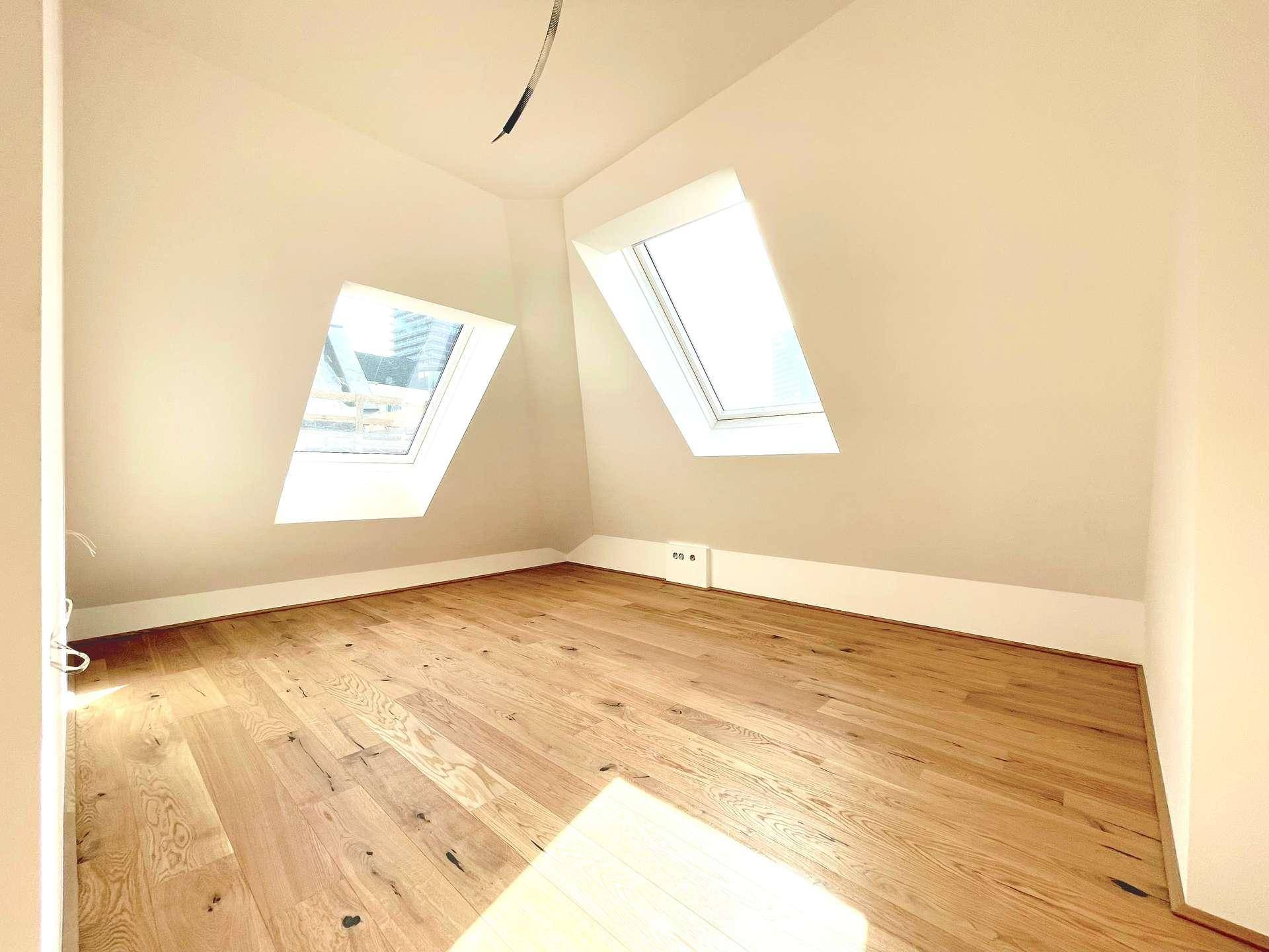 Helles Zimmer im Dachgeschoss mit Holzboden und zwei schrägen Dachfenstern, ideal als Schlaf- oder Arbeitszimmer.