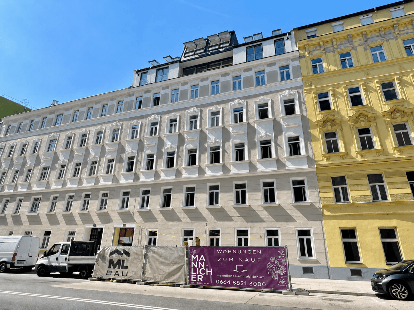 Historisches Gebäude mit moderner Dachaufstockung und Werbebanner für Wohnungen.