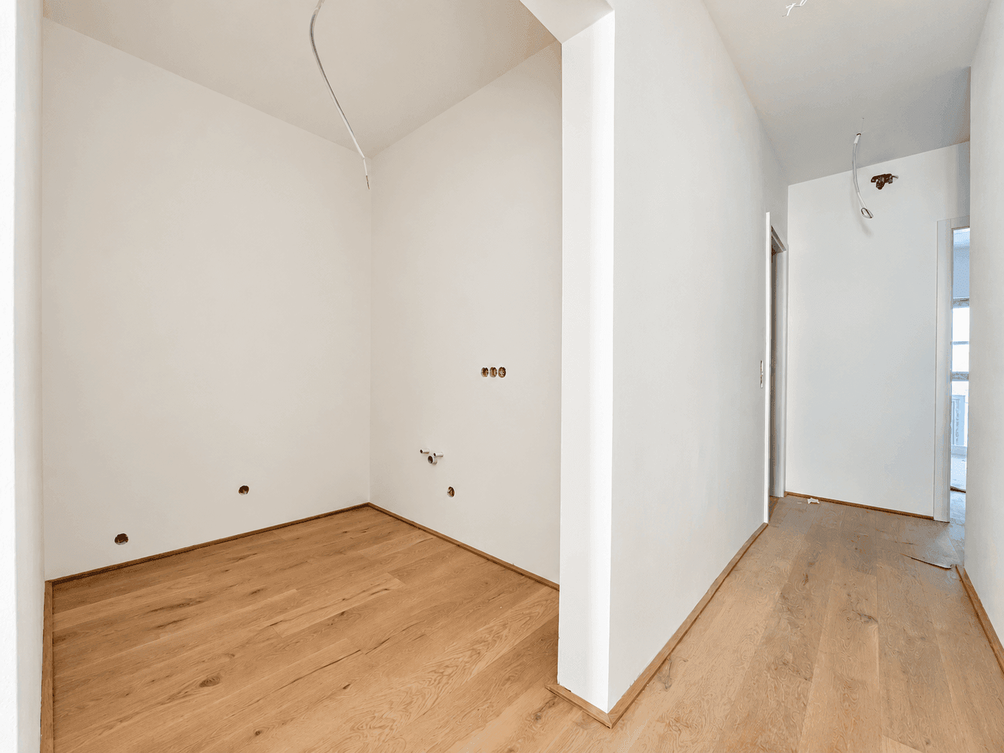 Kleiner Raum mit Anschlüssen und Holzboden, ideal als Abstellraum oder für eine Küchenzeile.