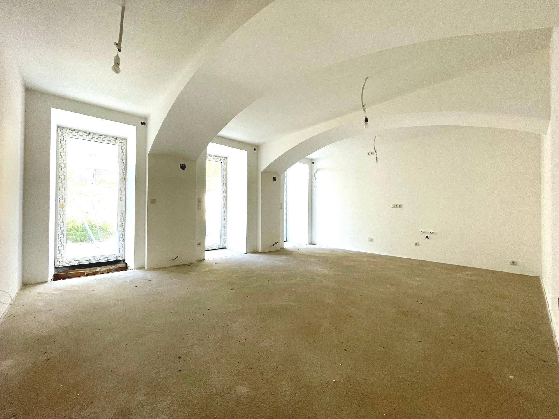Großer, heller Raum mit gewölbten Decken und mehreren Fenstertüren, noch im Rohbau.