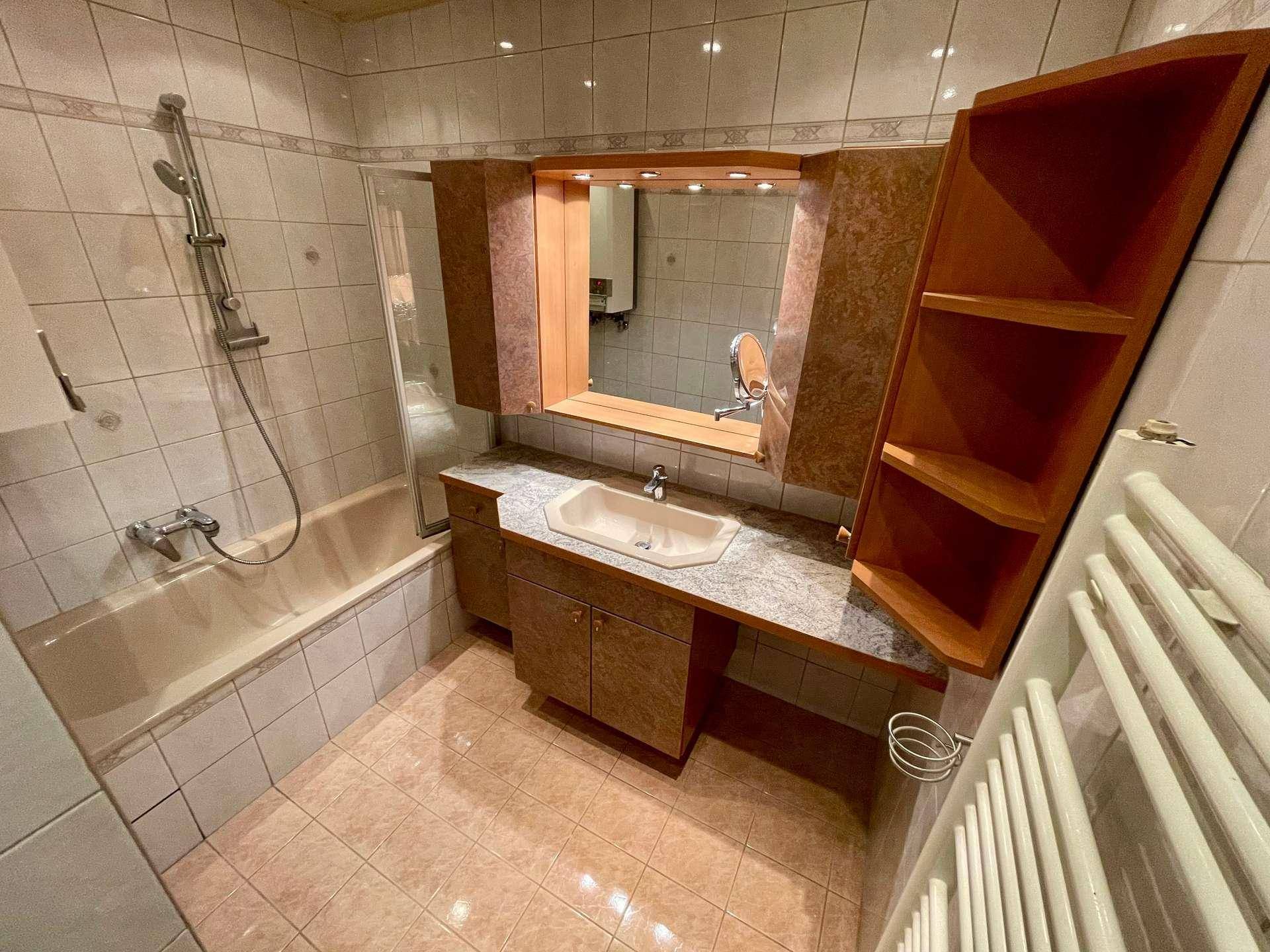 Badezimmer mit Badewanne, Waschbecken und Spiegelschrank, ausgestattet mit einem Handtuchheizkörper.
