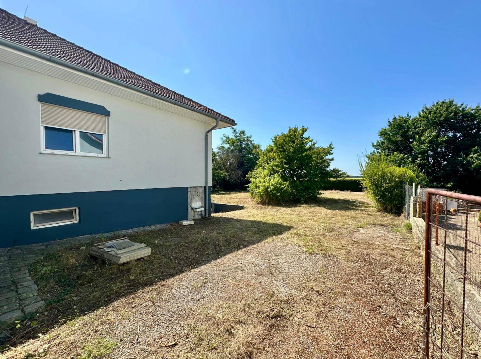 Seitenansicht des Hauses mit Blick auf den weitläufigen, naturbelassenen Gartenbereich und umliegende Bäume.