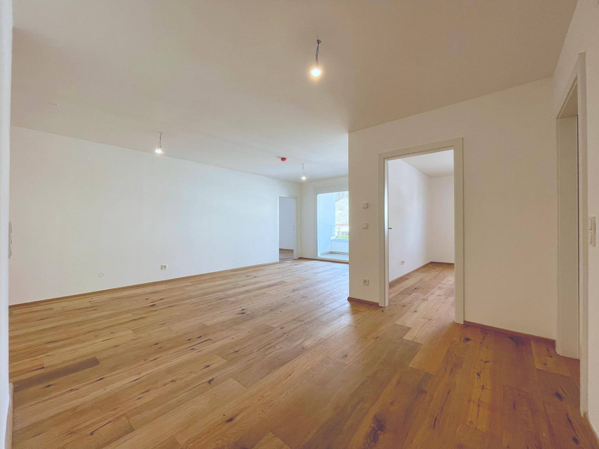 Helles Wohnzimmer mit Holzboden und Zugang zu weiteren Räumen, ideal für offenes Wohnen.