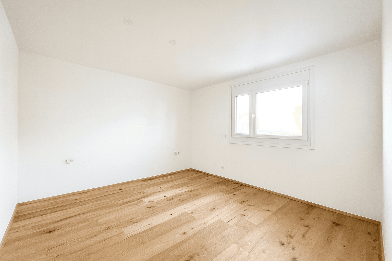 Helles Schlafzimmer mit Holzboden und einem Fenster, das viel Tageslicht in den Raum bringt.