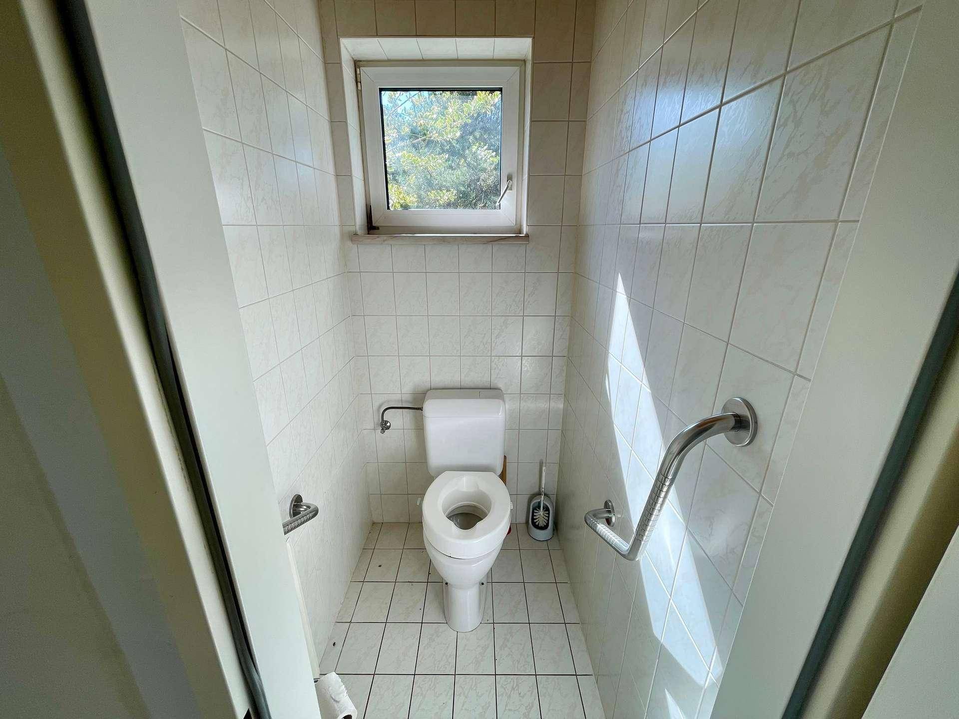 Separates WC mit Fenster, Fliesenboden und Haltegriffen für zusätzliche Sicherheit.