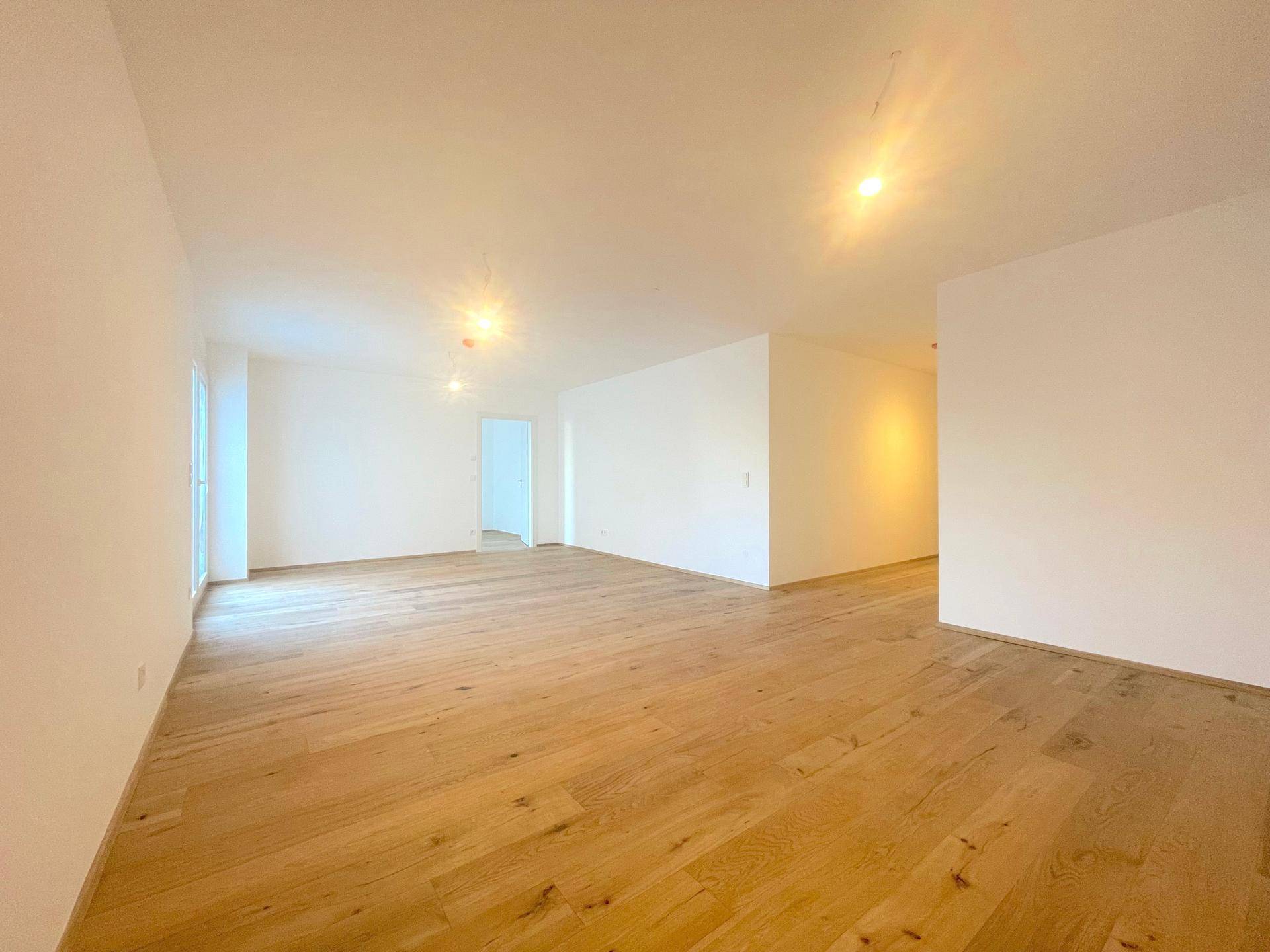 Lichtdurchflutetes Wohnzimmer mit Holzboden und großen Fenstern, bietet eine angenehme Wohnatmosphäre.