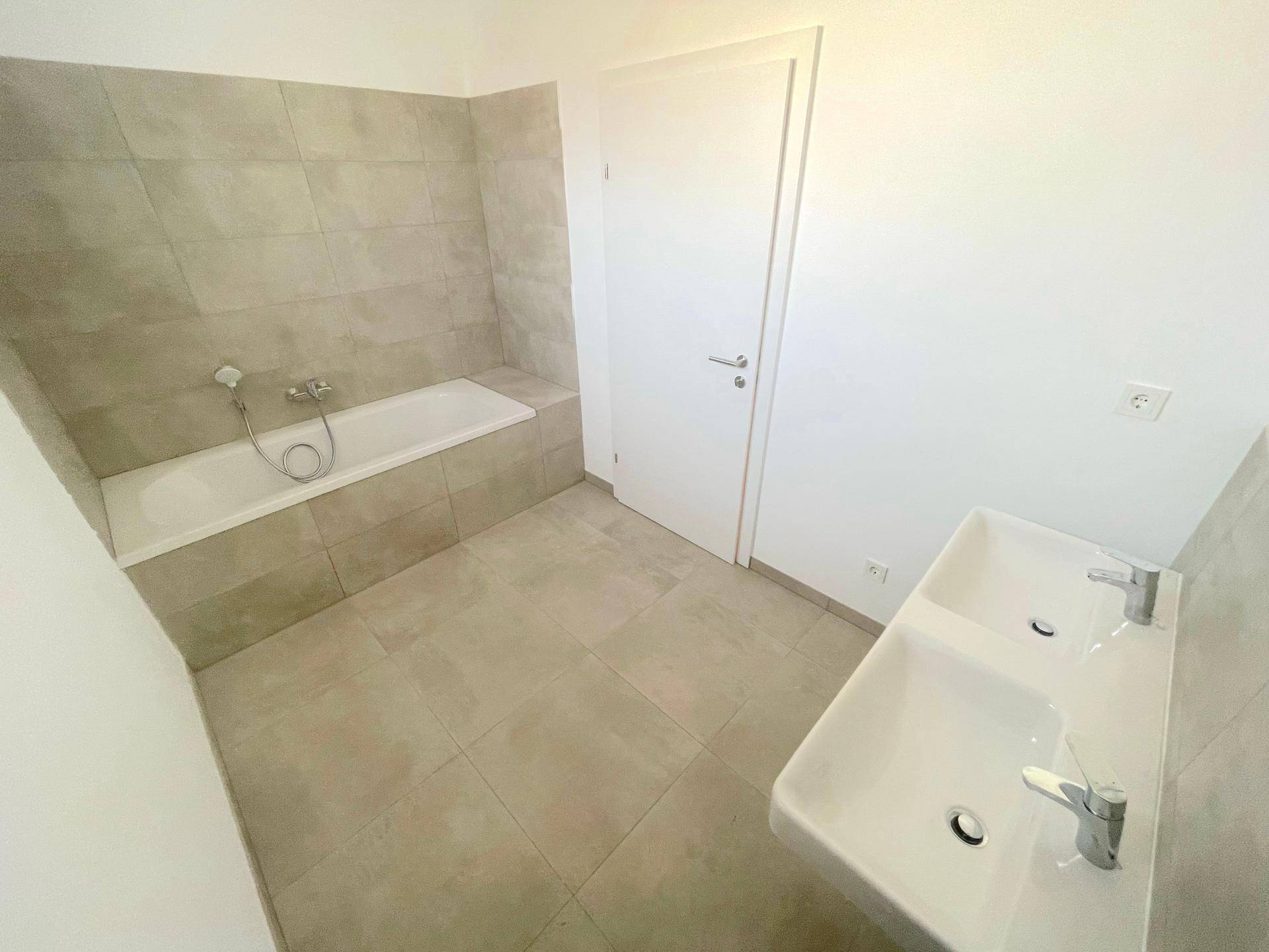 Modernes Badezimmer mit Badewanne, Doppelwaschbecken und hellen Fliesen.