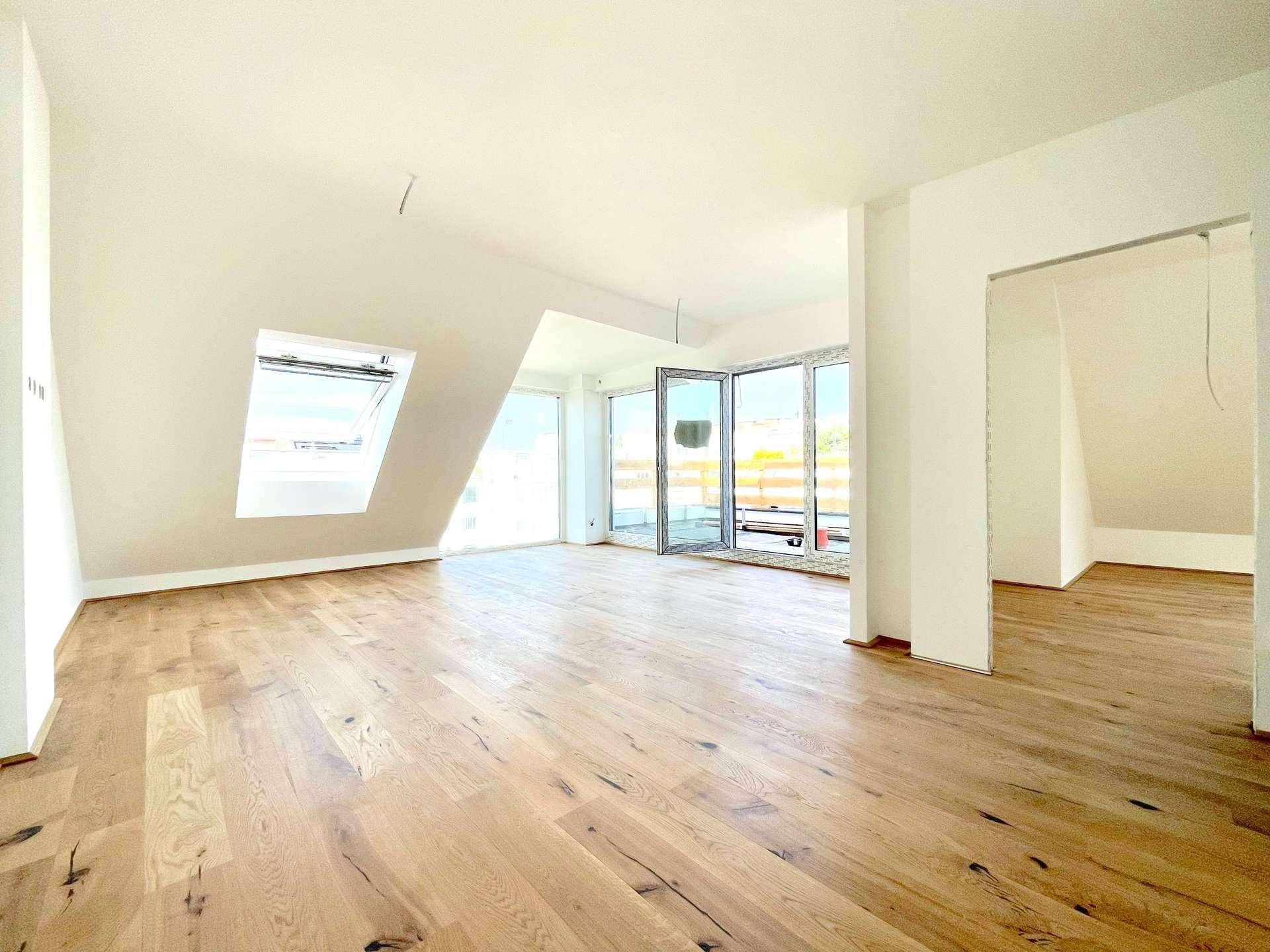 Helles, geräumiges Wohnzimmer im Dachgeschoss mit Holzboden, Dachfenstern und Zugang zu einem Balkon.