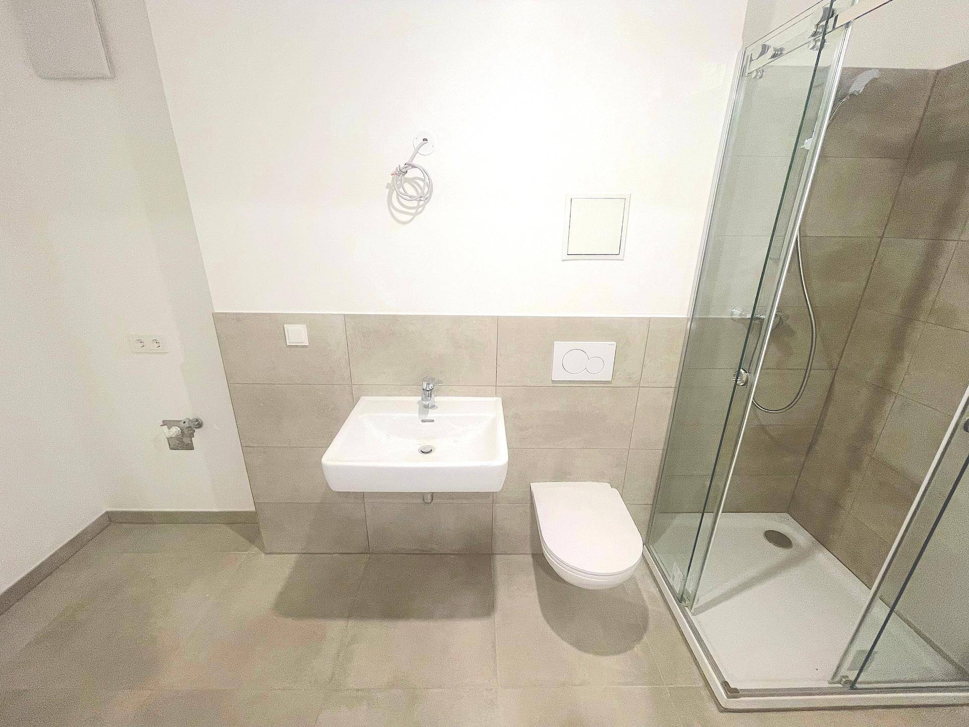 Modernes Badezimmer mit Duschkabine, wandhängendem WC und hellem Fliesenboden.