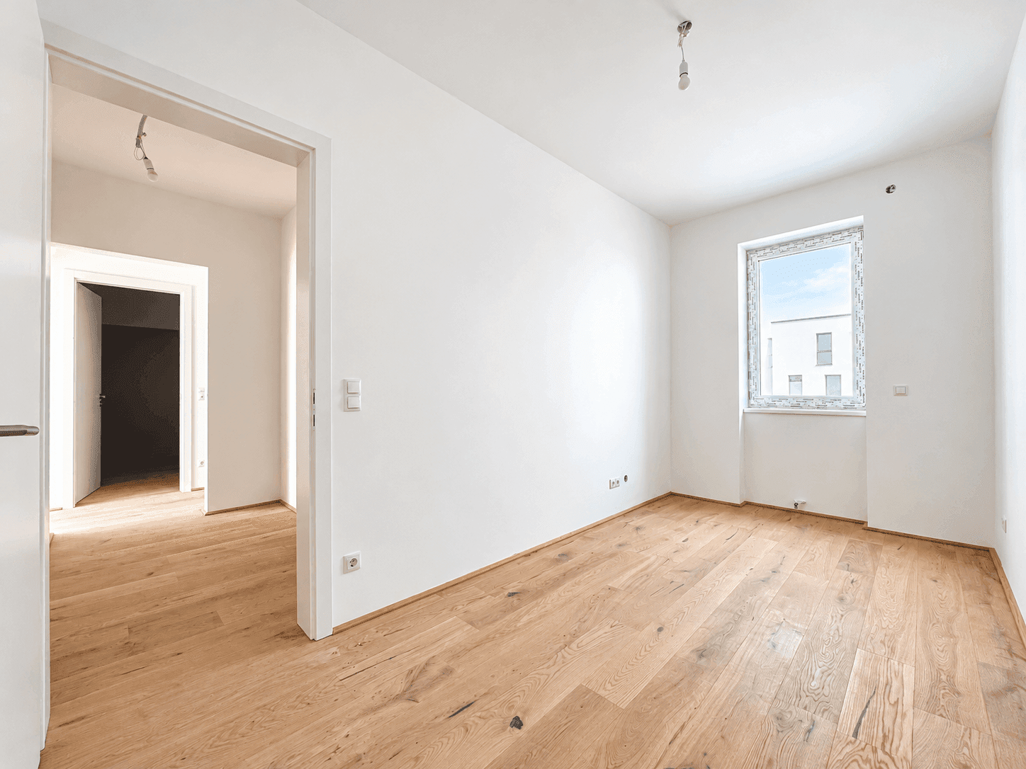 Helles Zimmer mit Eichenparkett und einem Fenster, ideal als Kinder- oder Arbeitszimmer.